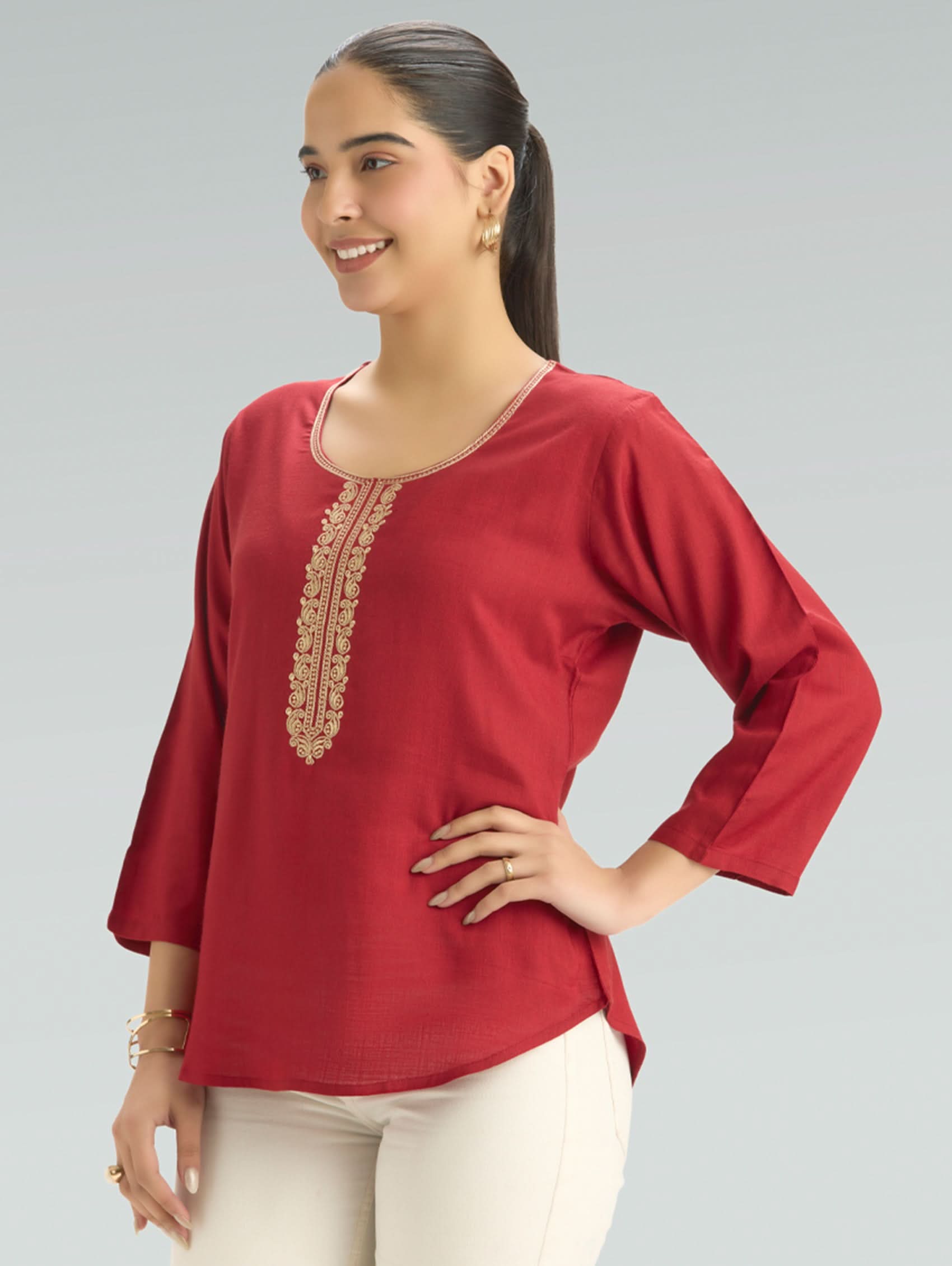 Woman wearing a red top with gold embroidery on a gray background