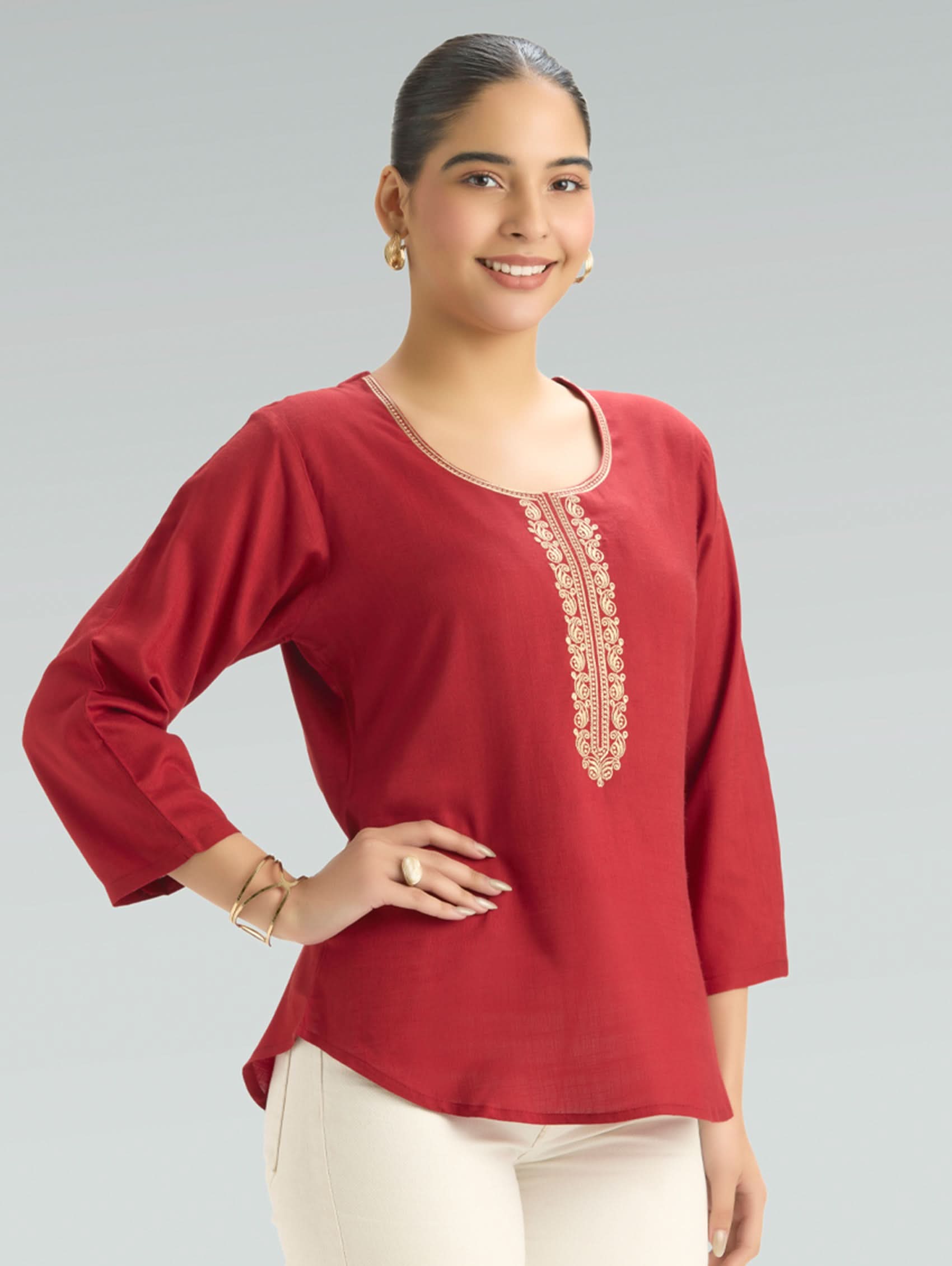 Woman wearing a red blouse with gold embroidery on a gray background