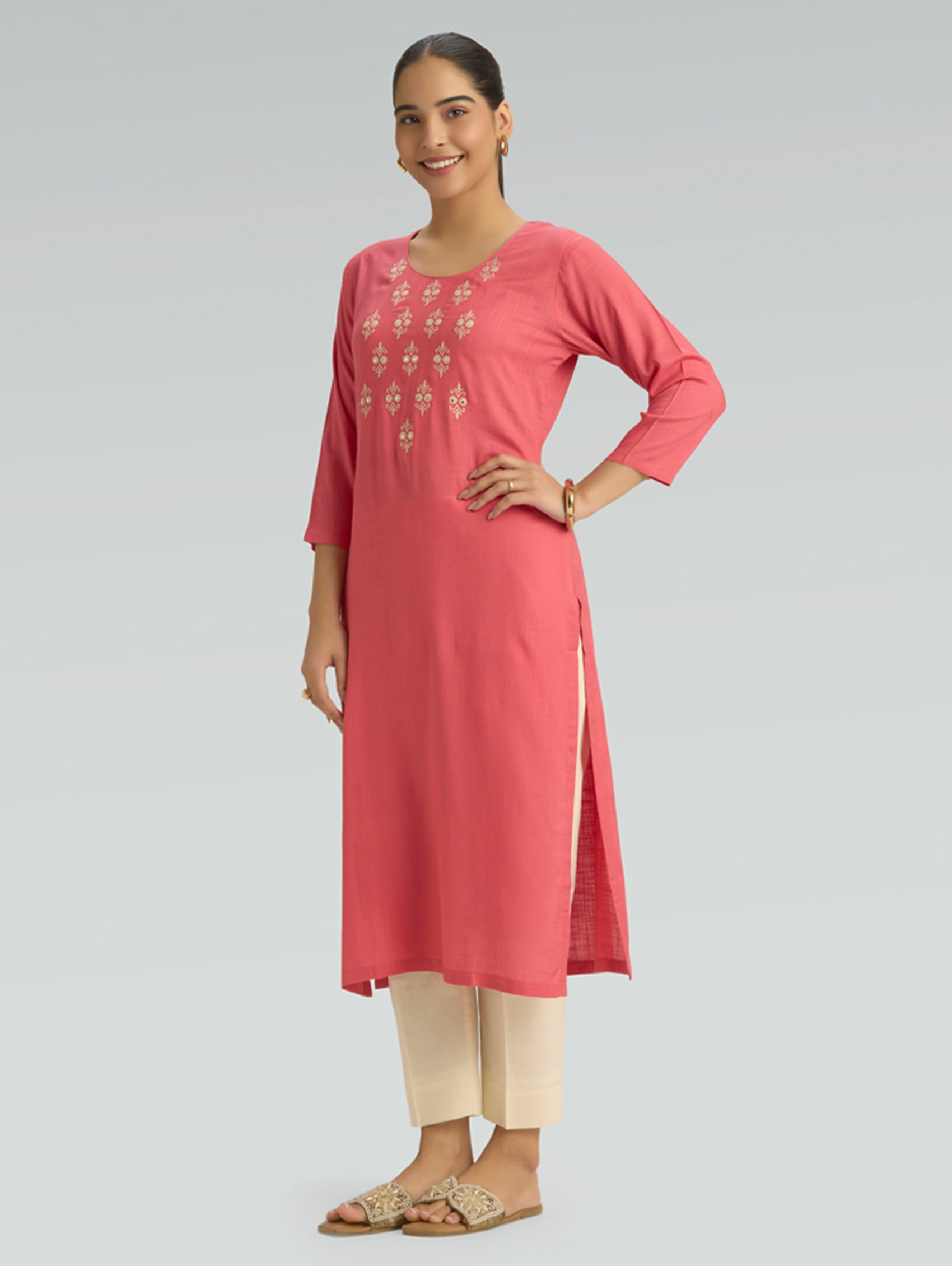Woman wearing a coral pink kurta with beige pants on a gray background