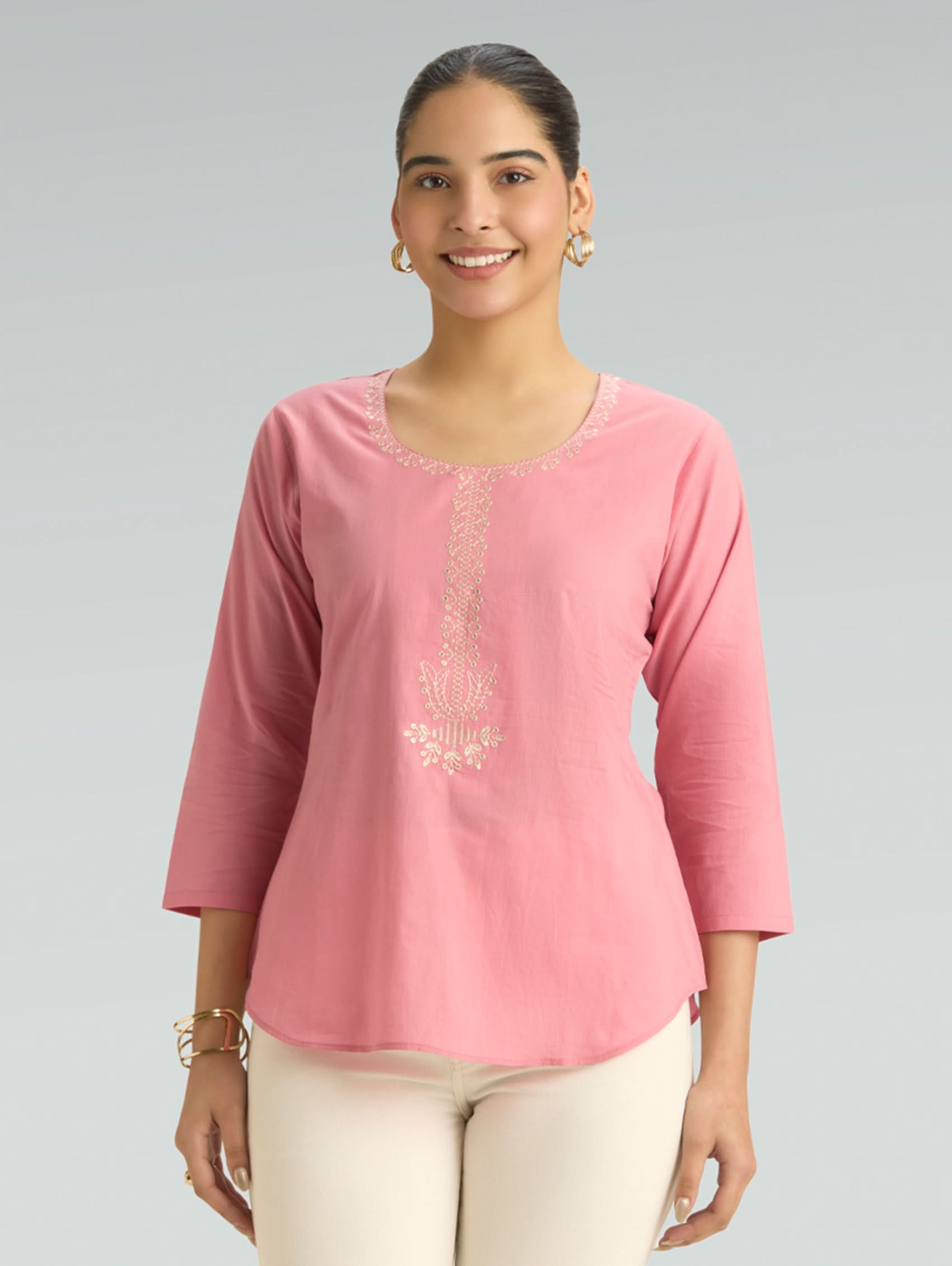 Woman wearing a pink top with lace details on a gray background