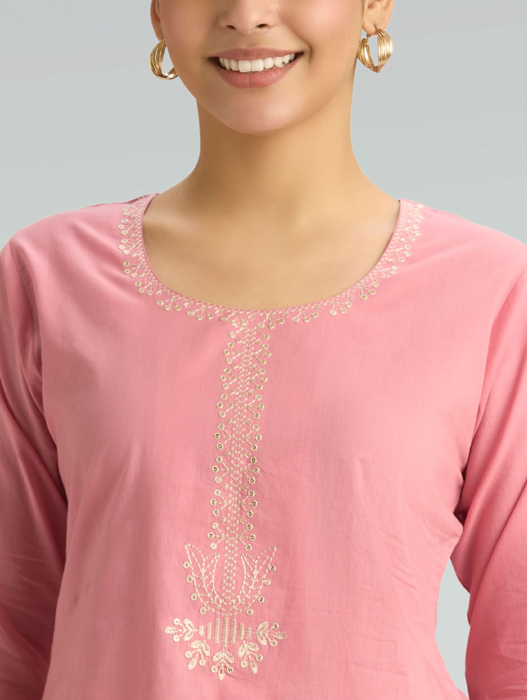 Close-up of a pink top with gold embroidery on a gray background