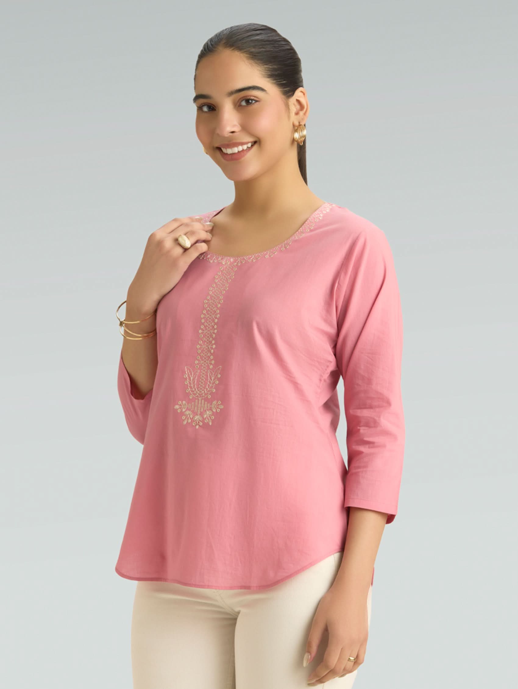Woman wearing a pink top with embroidery on a gray background