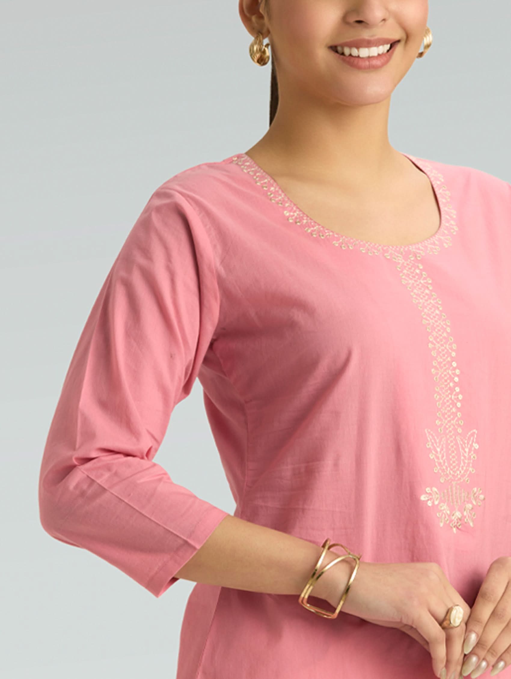 Woman wearing a pink kurta with white embroidery on a light gray background