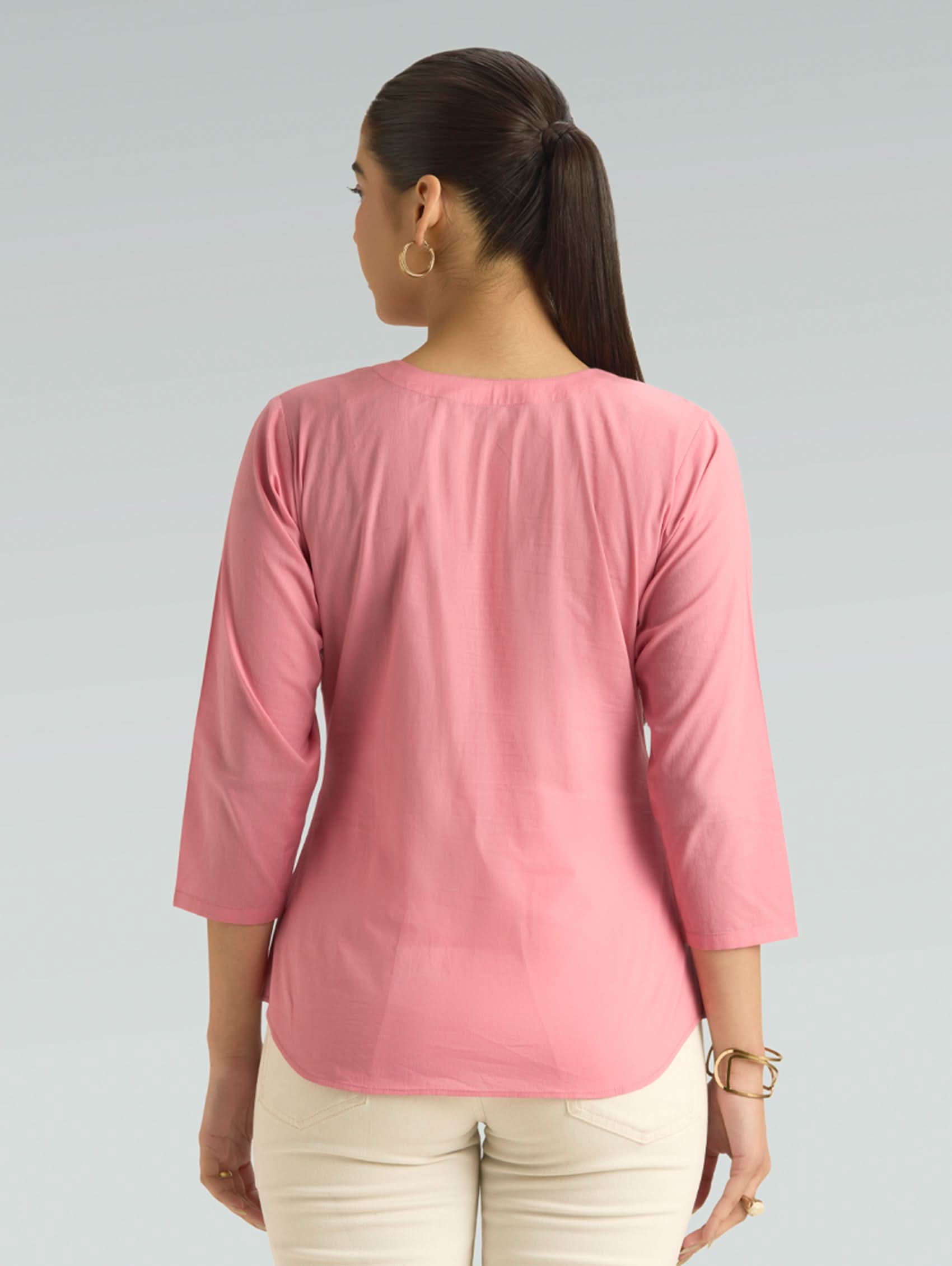 Woman wearing a pink top with three-quarter sleeves on a gray background