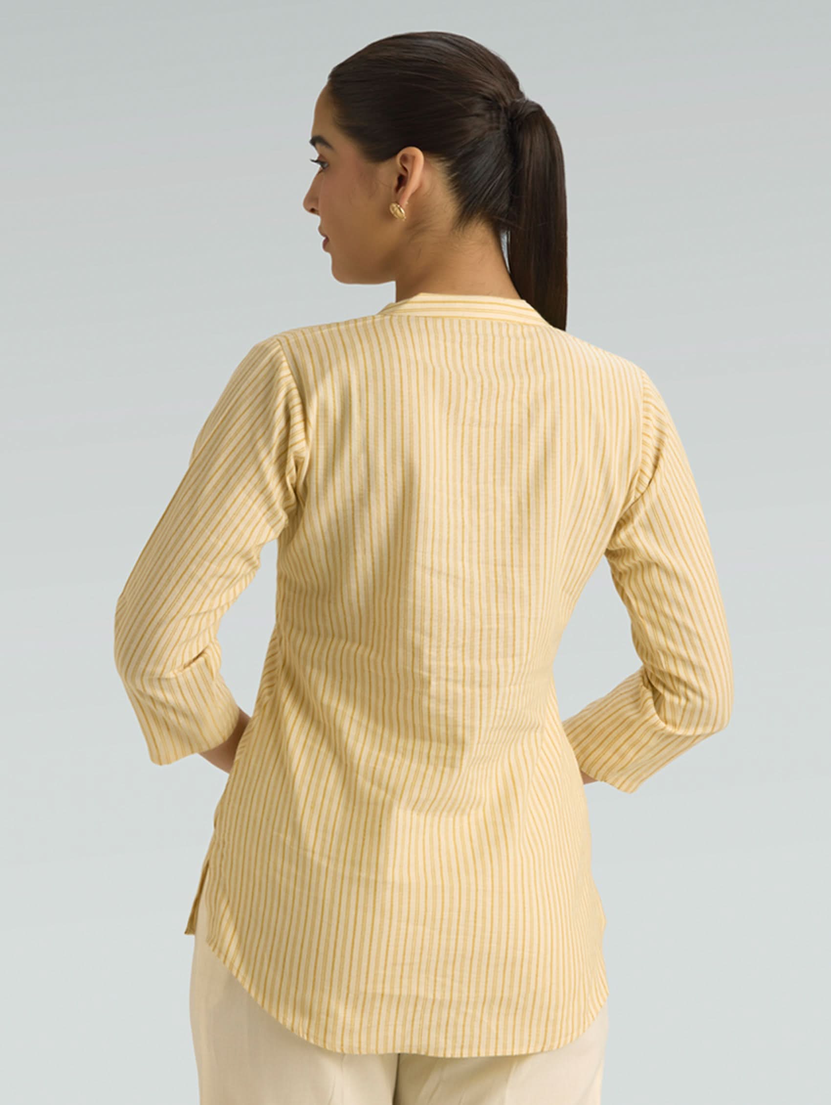 Woman wearing a yellow ribbed long-sleeve top against a gray background