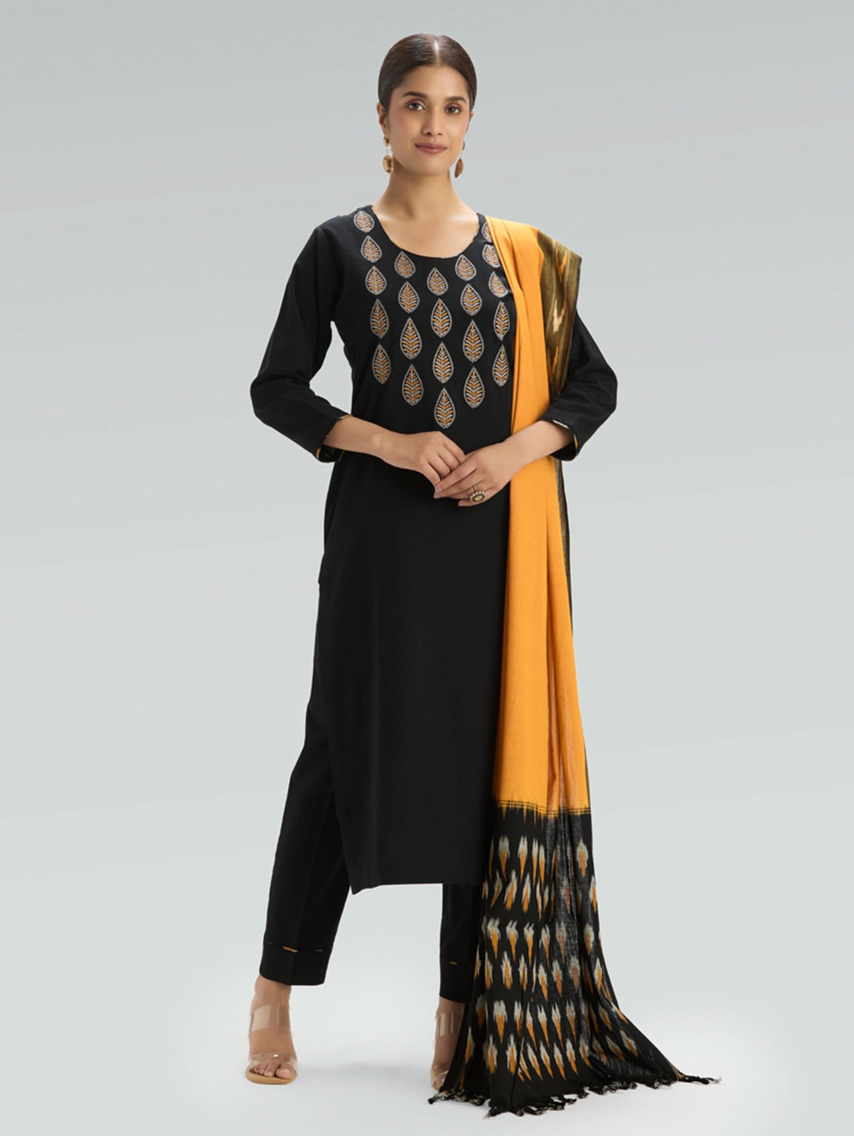 Woman wearing a black kurta with a yellow and black dupatta on a gray background