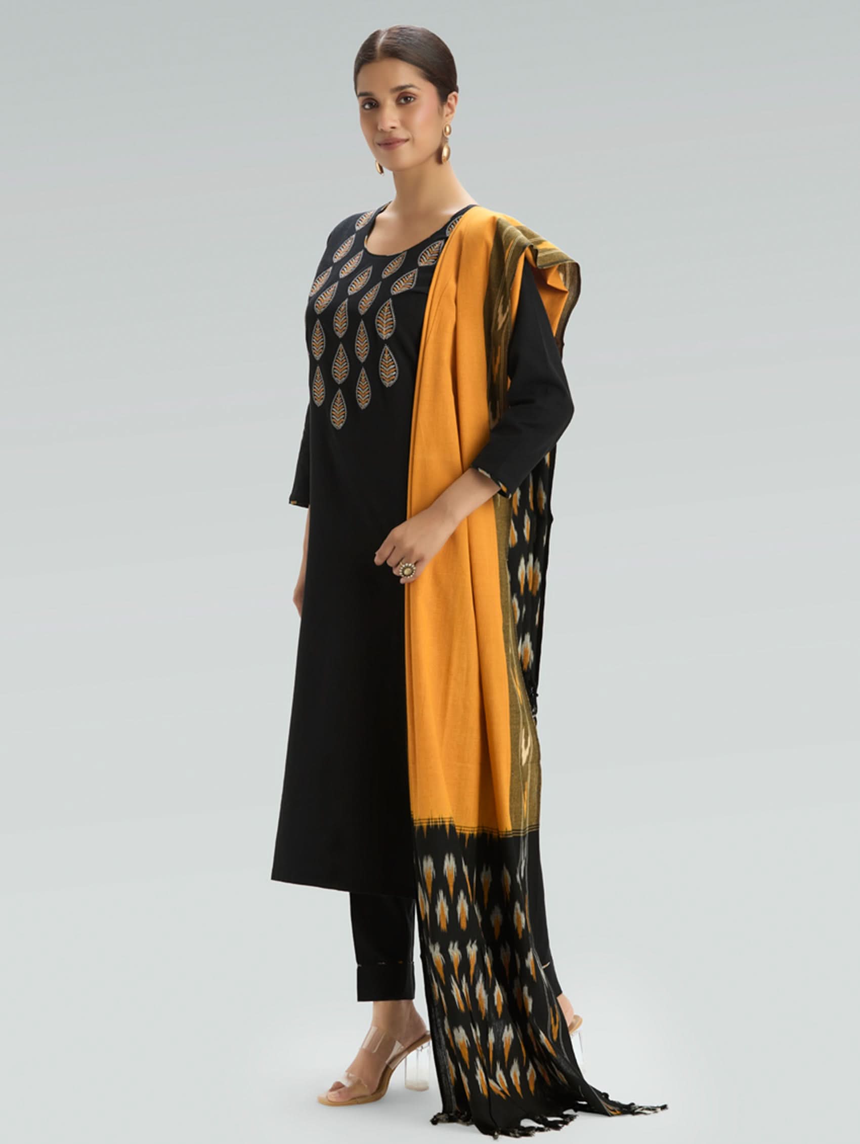 Woman wearing a black and yellow traditional outfit with a scarf on a gray background