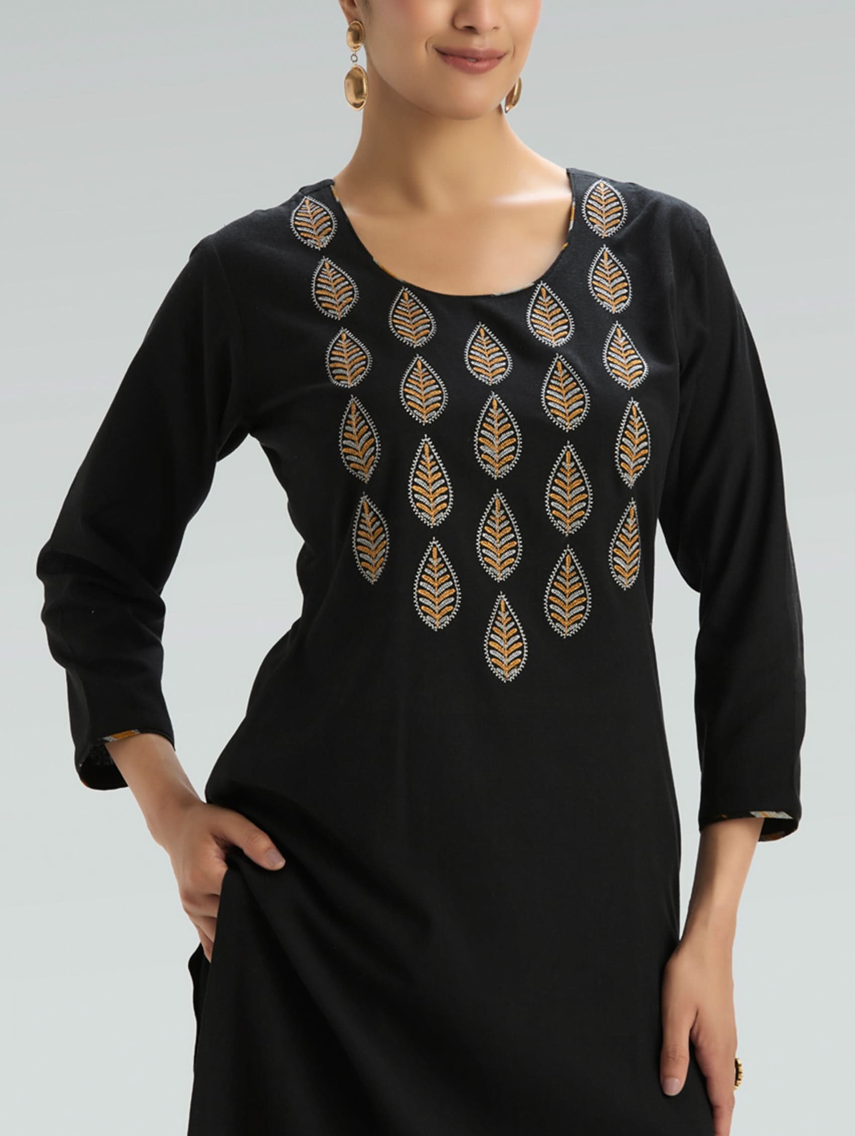 Black dress with gold leaf patterns worn by a model on a gray background