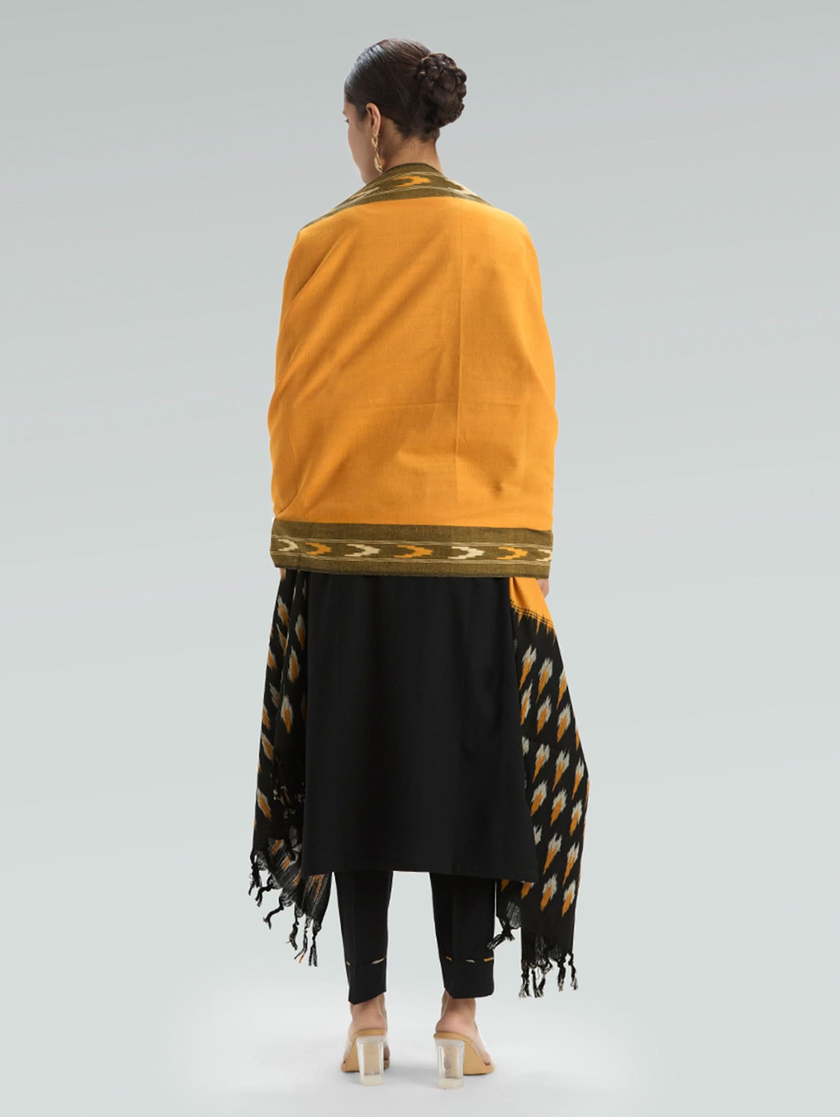 Woman wearing a mustard yellow top and black patterned skirt on a light gray background