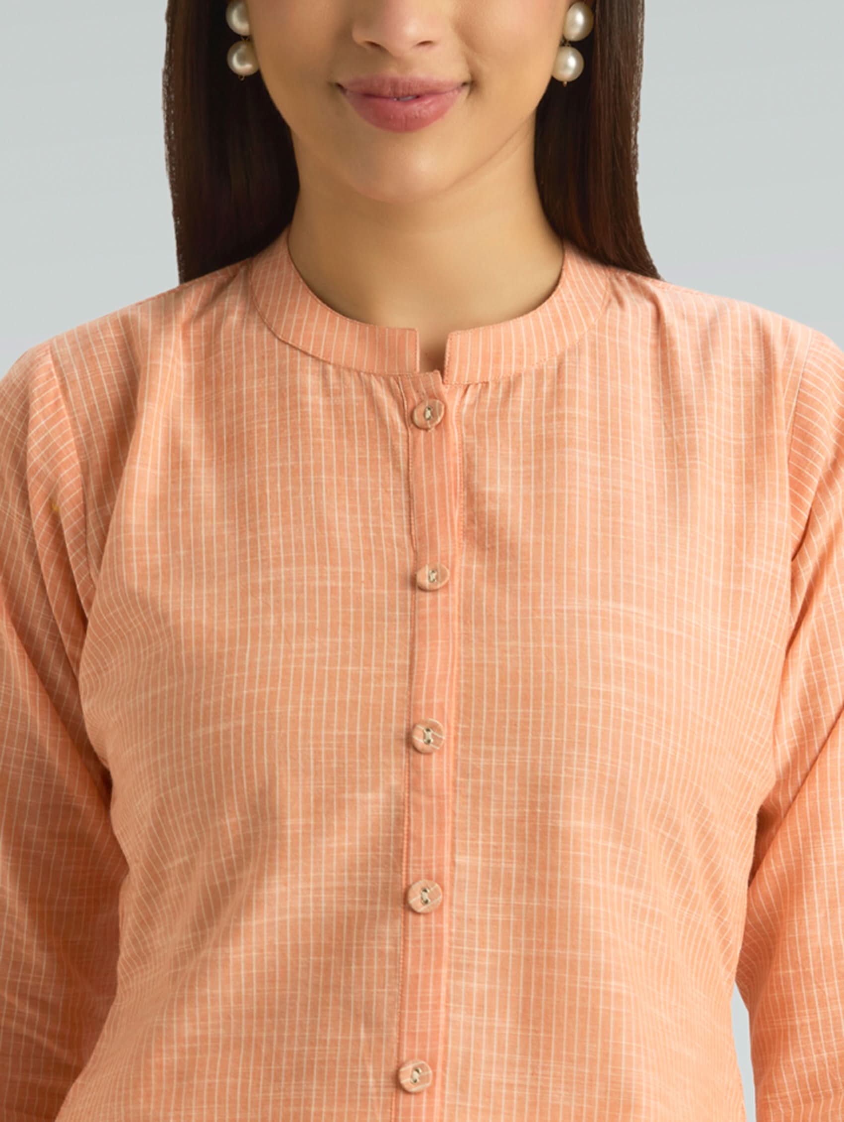 Woman wearing a peach-colored checkered shirt against a neutral background