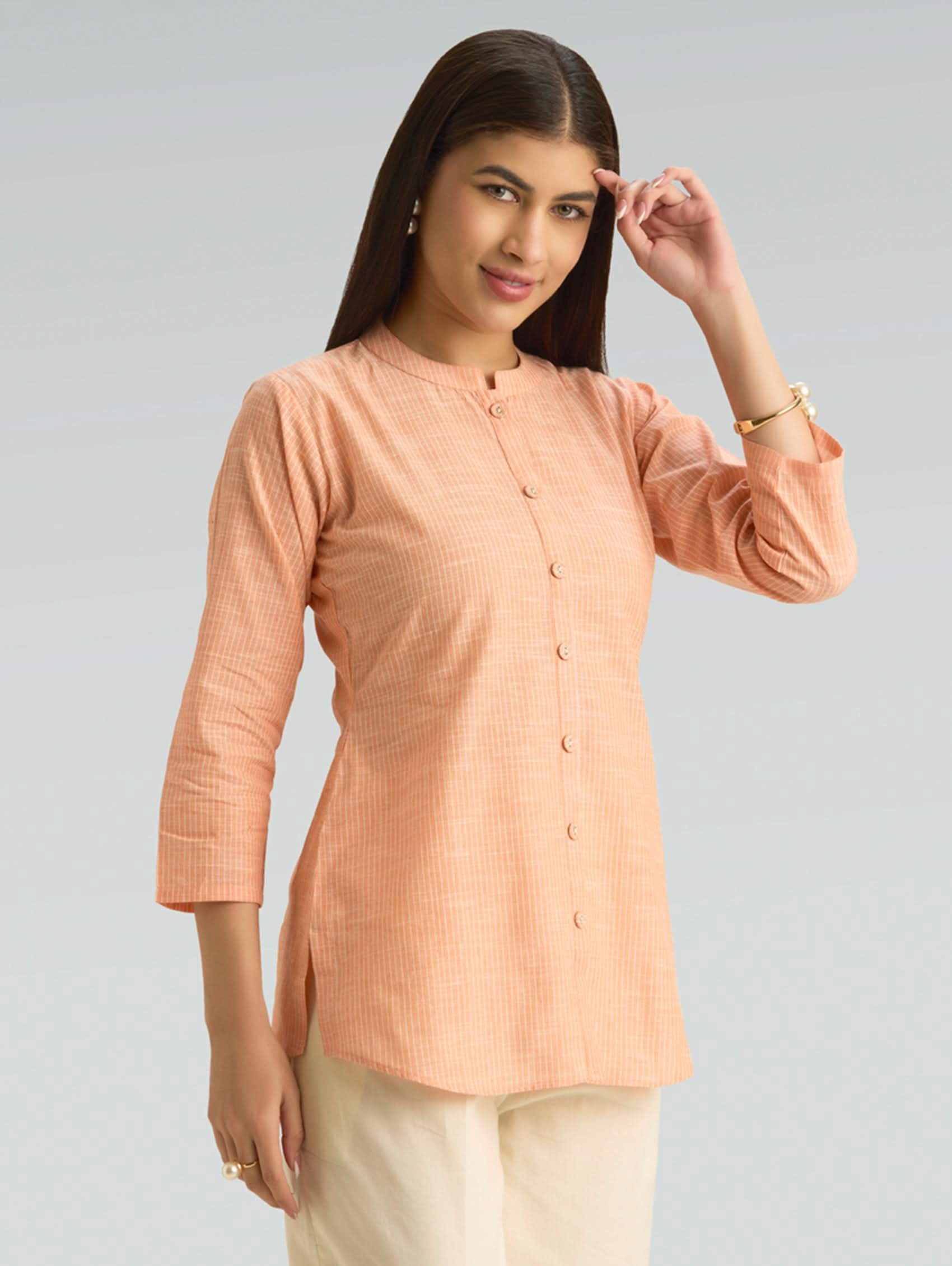 Woman wearing a peach-colored long-sleeve top against a gray background