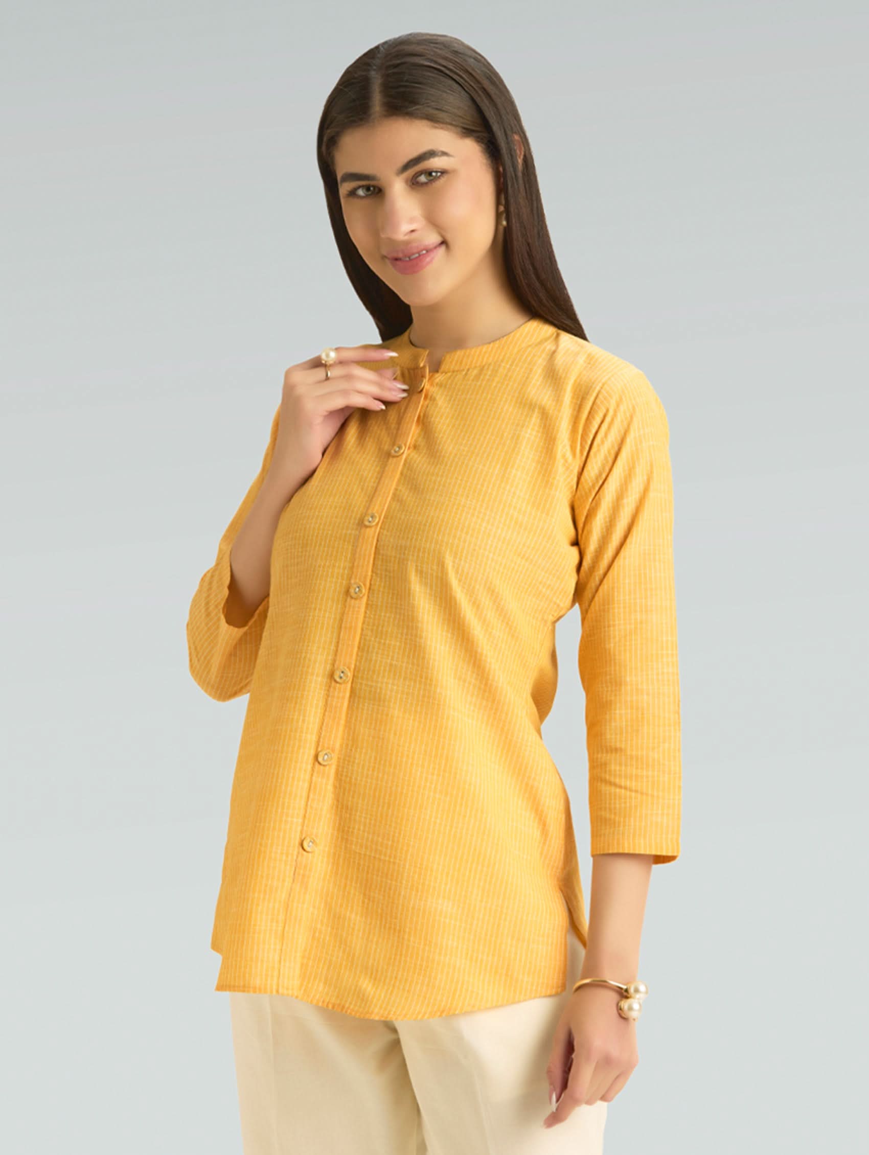 Woman wearing a yellow kurta with beige pants on a gray background