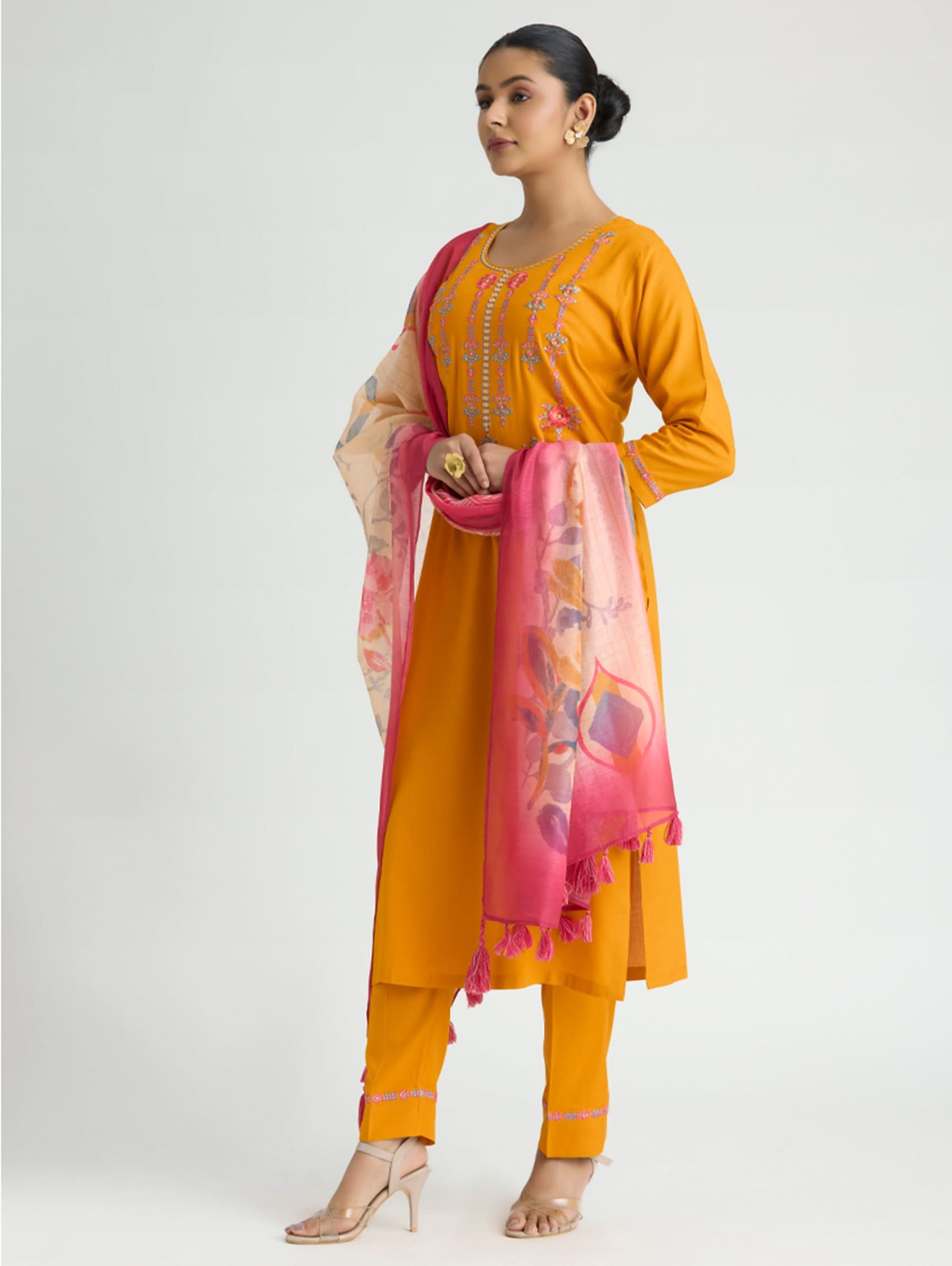 Woman wearing a mustard yellow kurta with pink dupatta on a white background