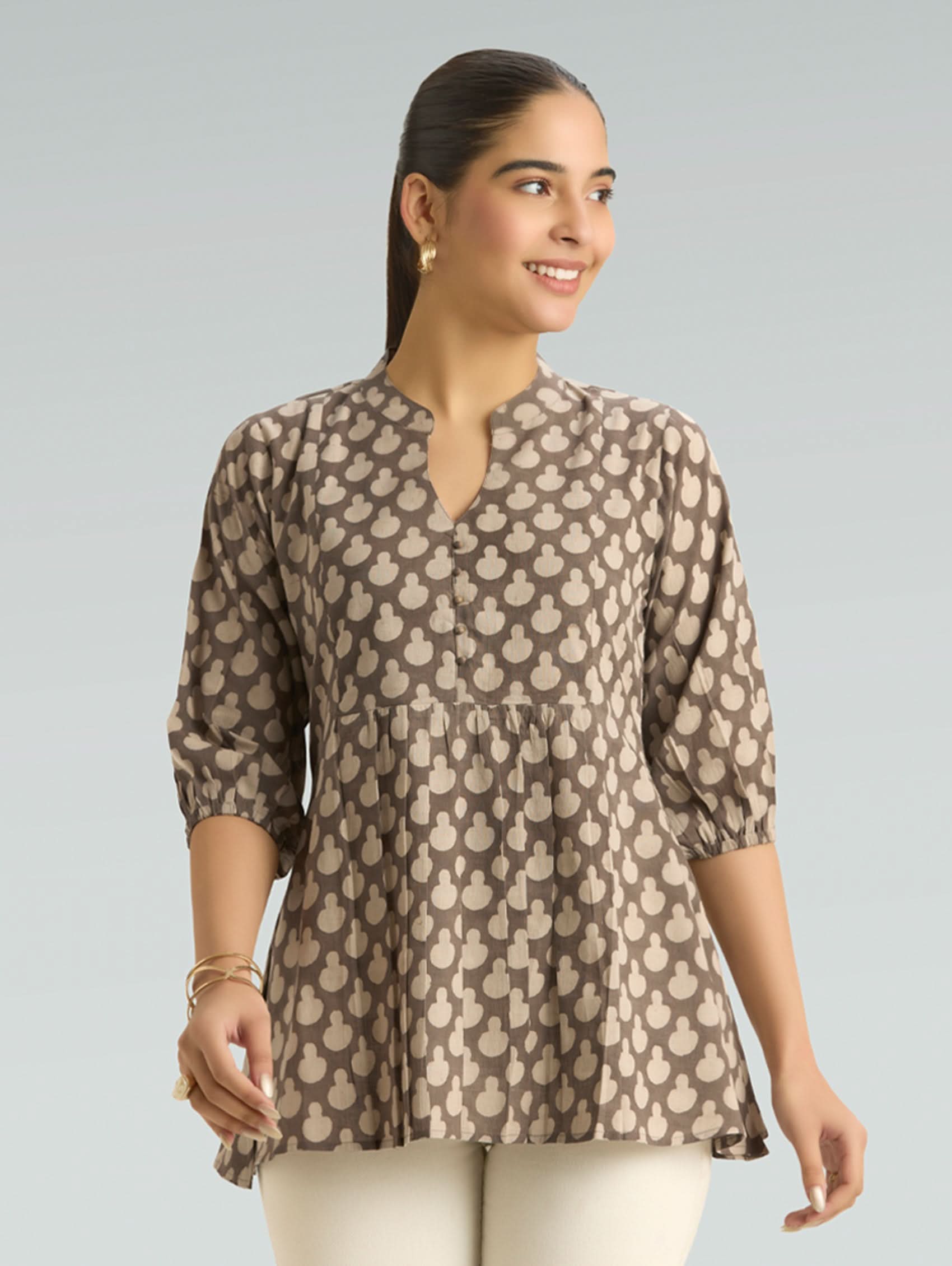 Woman wearing a patterned brown blouse against a gray background