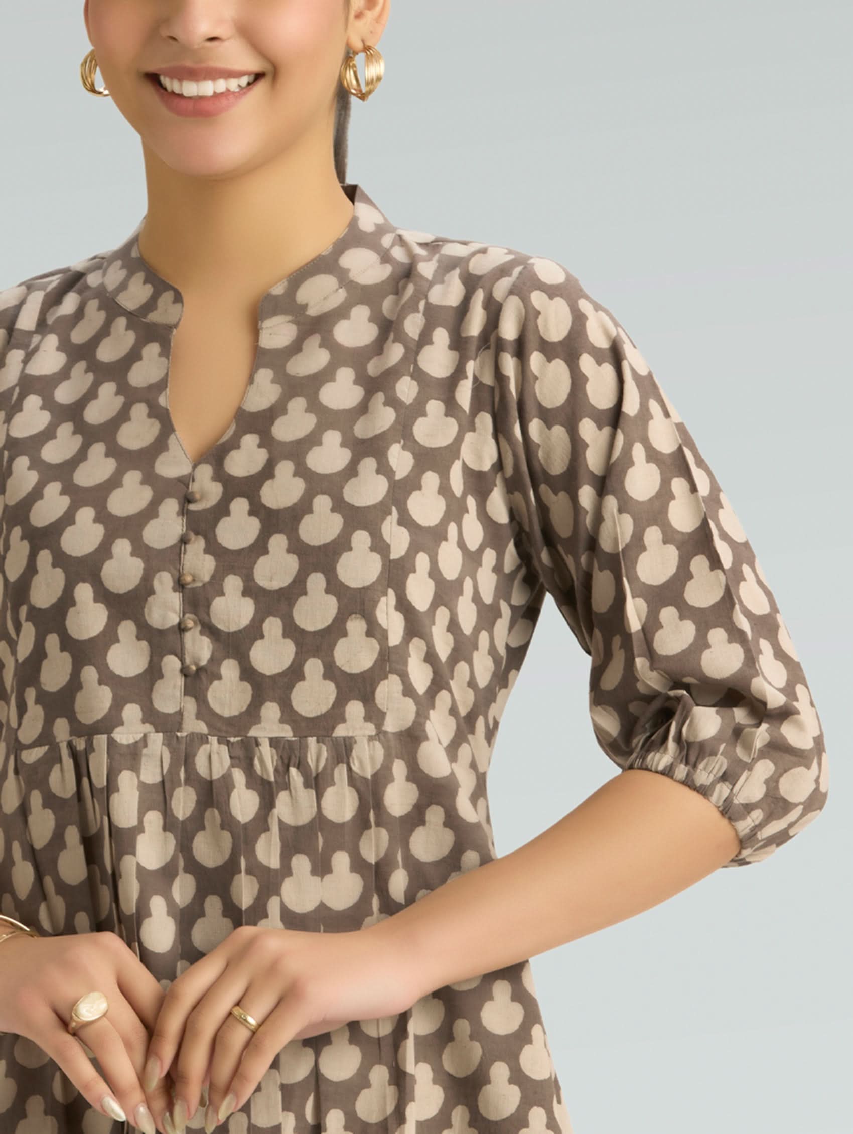 Woman wearing a brown and beige patterned dress on a light gray background
