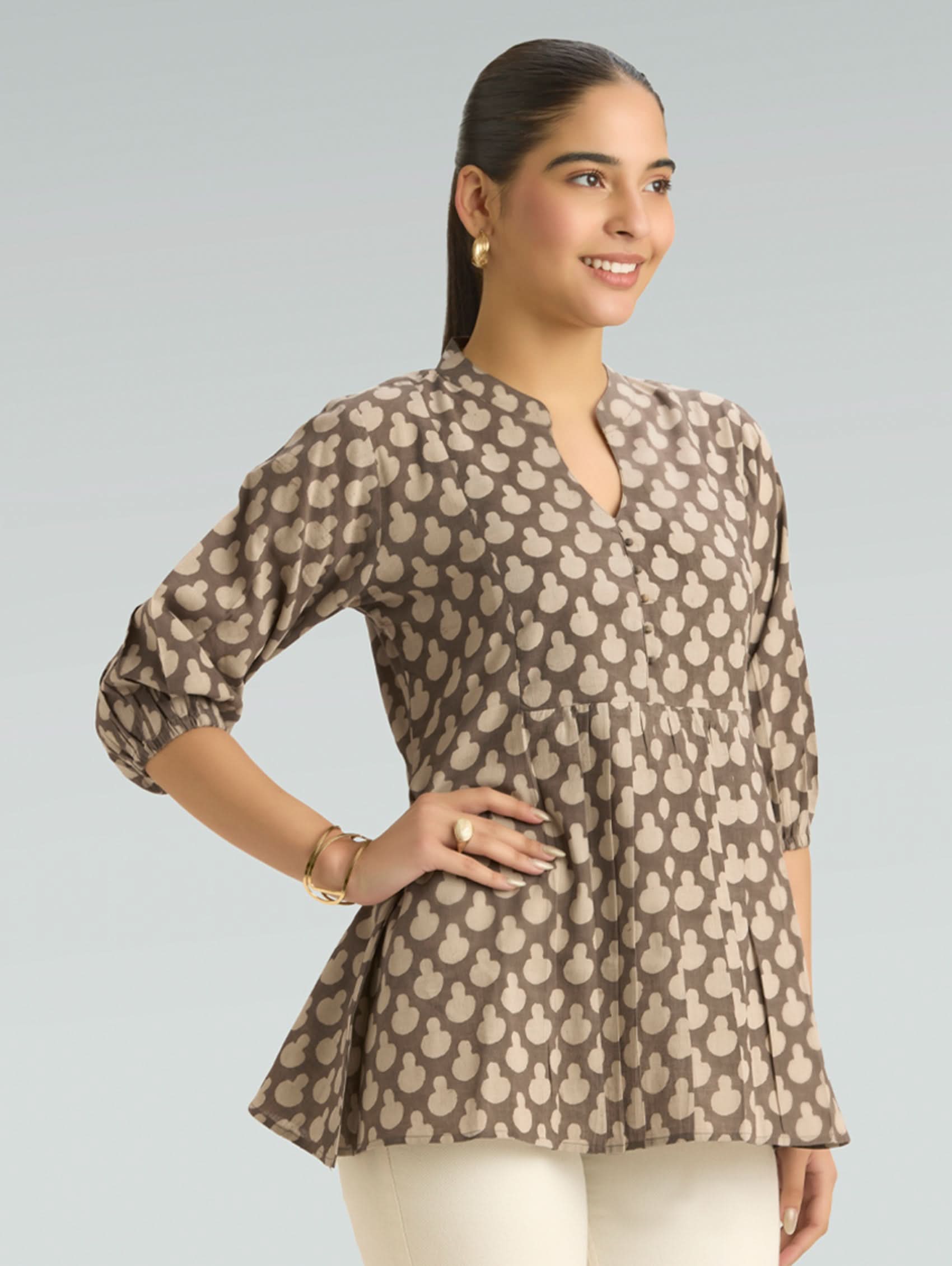 Woman wearing a patterned brown blouse against a gray background