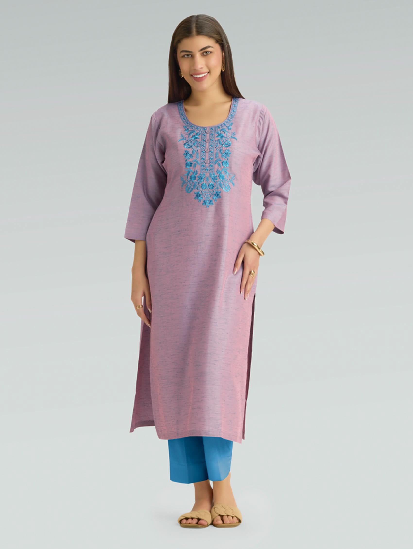 Woman wearing a pink kurta with blue embroidery and blue pants on a gray background