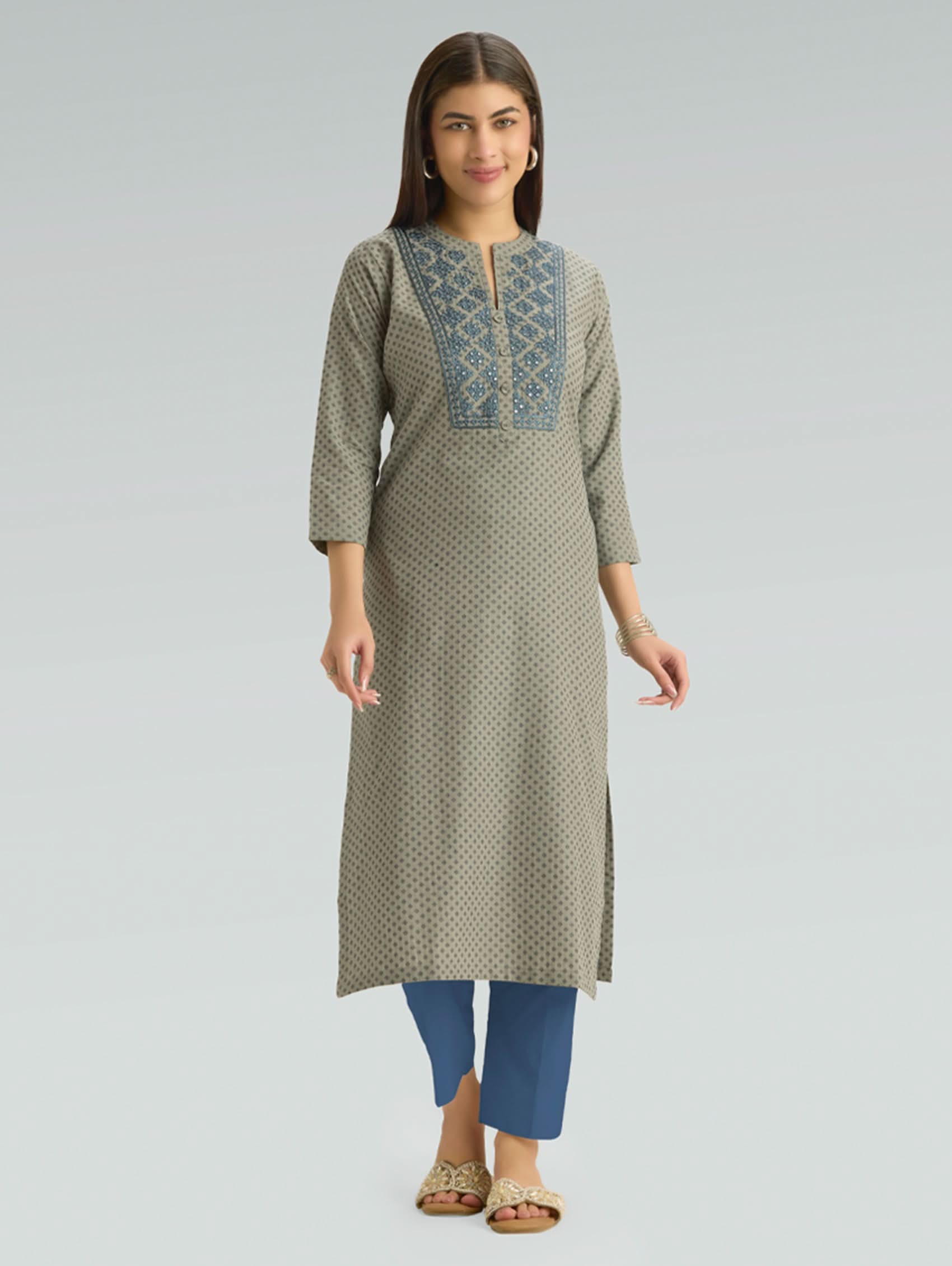 Woman wearing a long green patterned dress with blue accents on a gray background