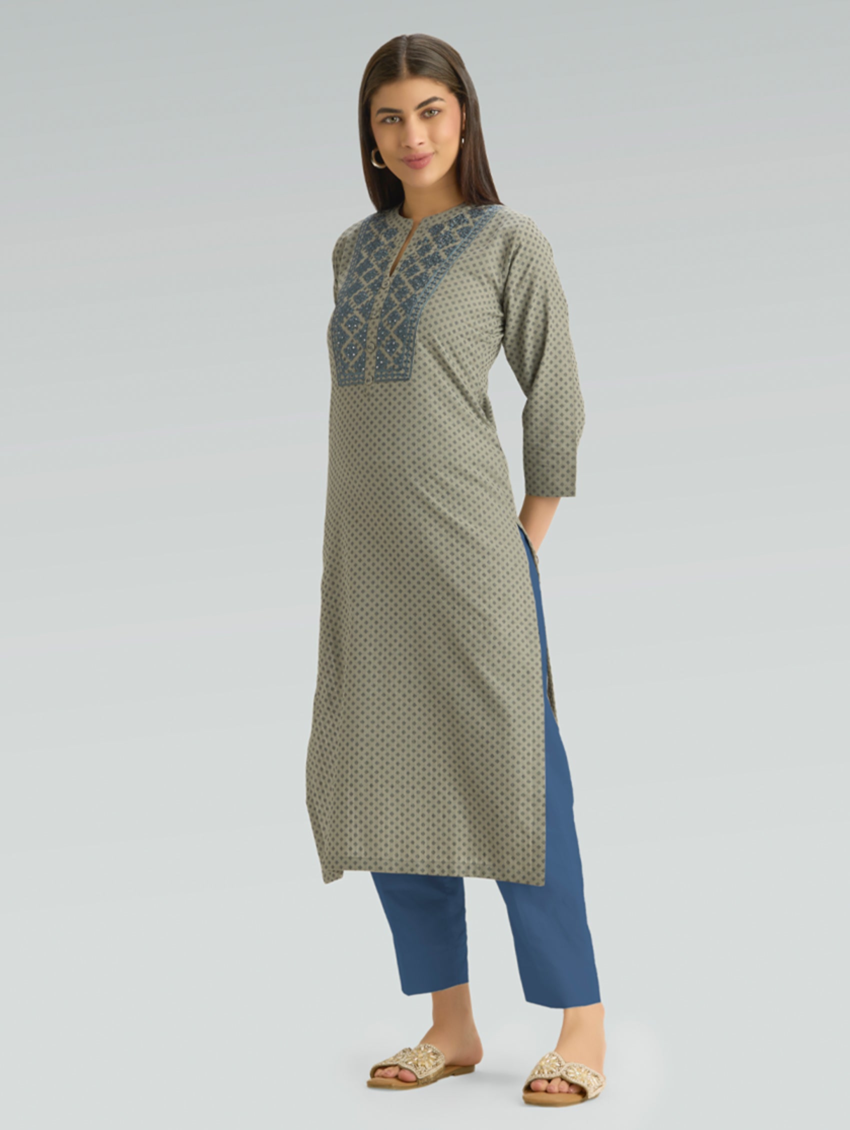 Woman wearing a green patterned kurta with blue pants on a light gray background