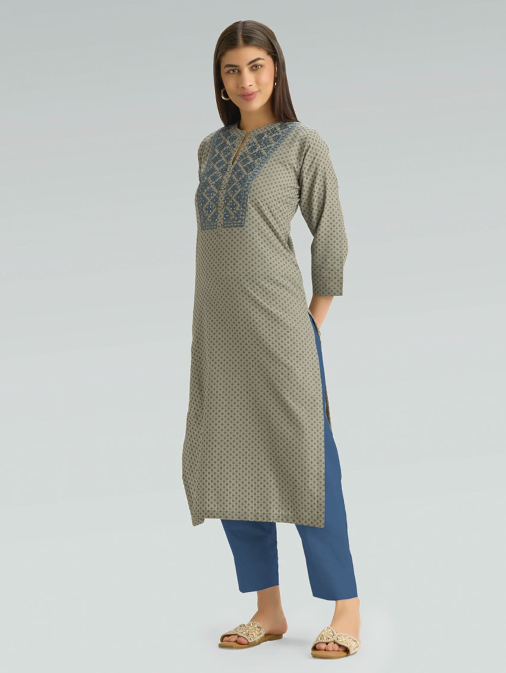 Woman wearing a green patterned kurta with blue pants on a light gray background