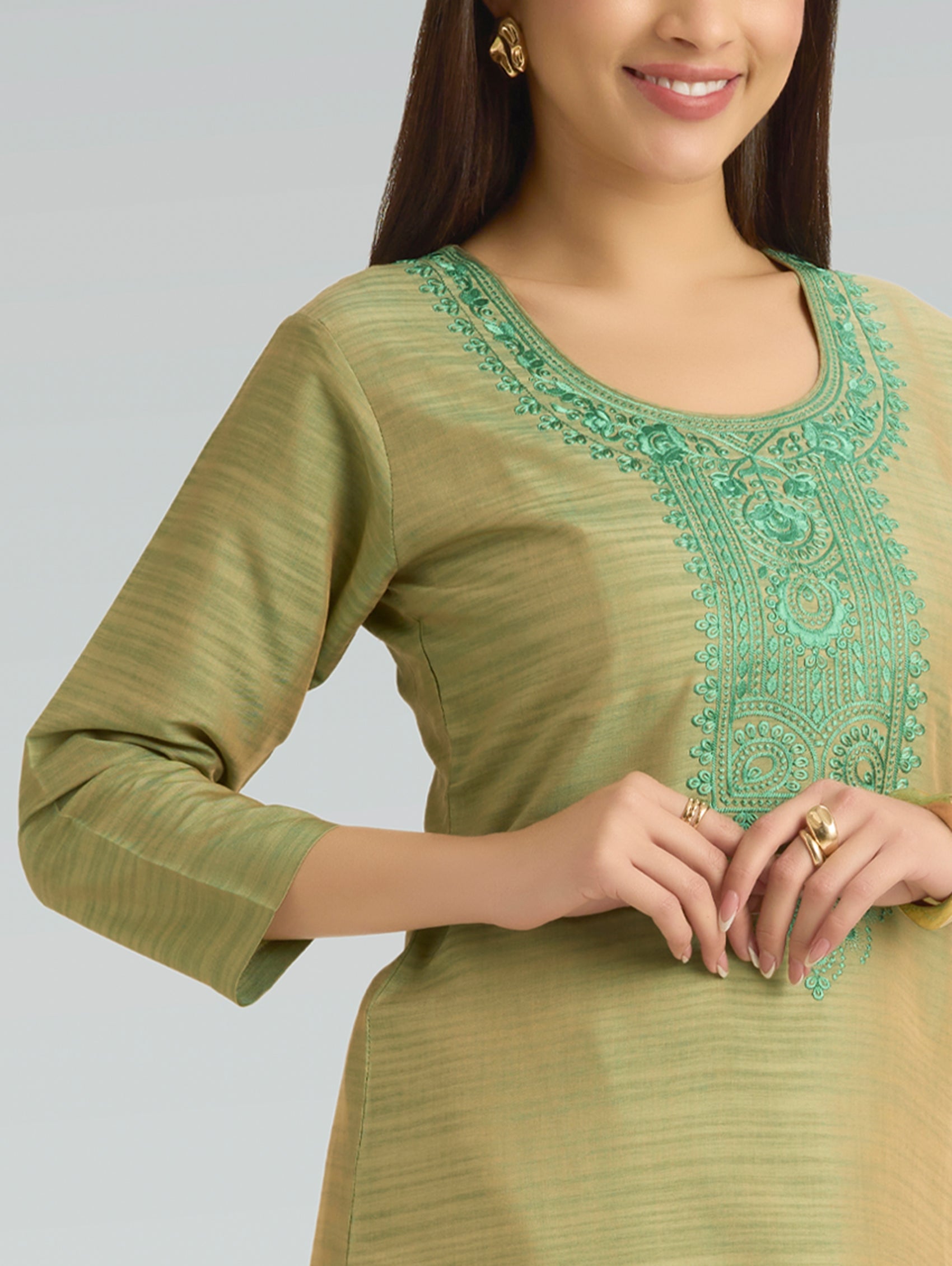 Woman wearing a green embroidered top against a gray background