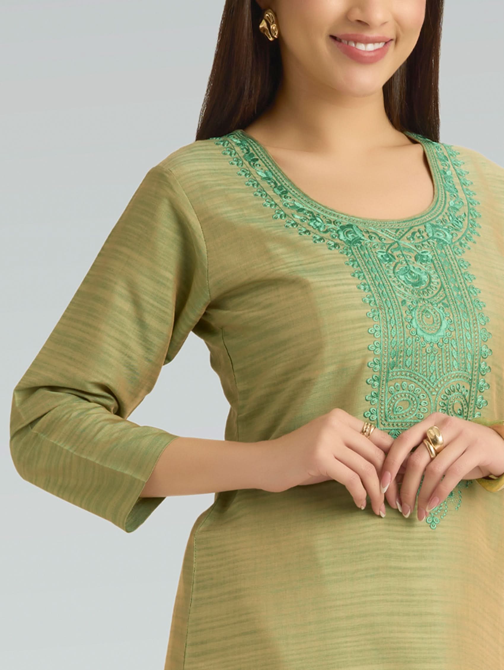 Woman wearing a green embroidered top against a gray background