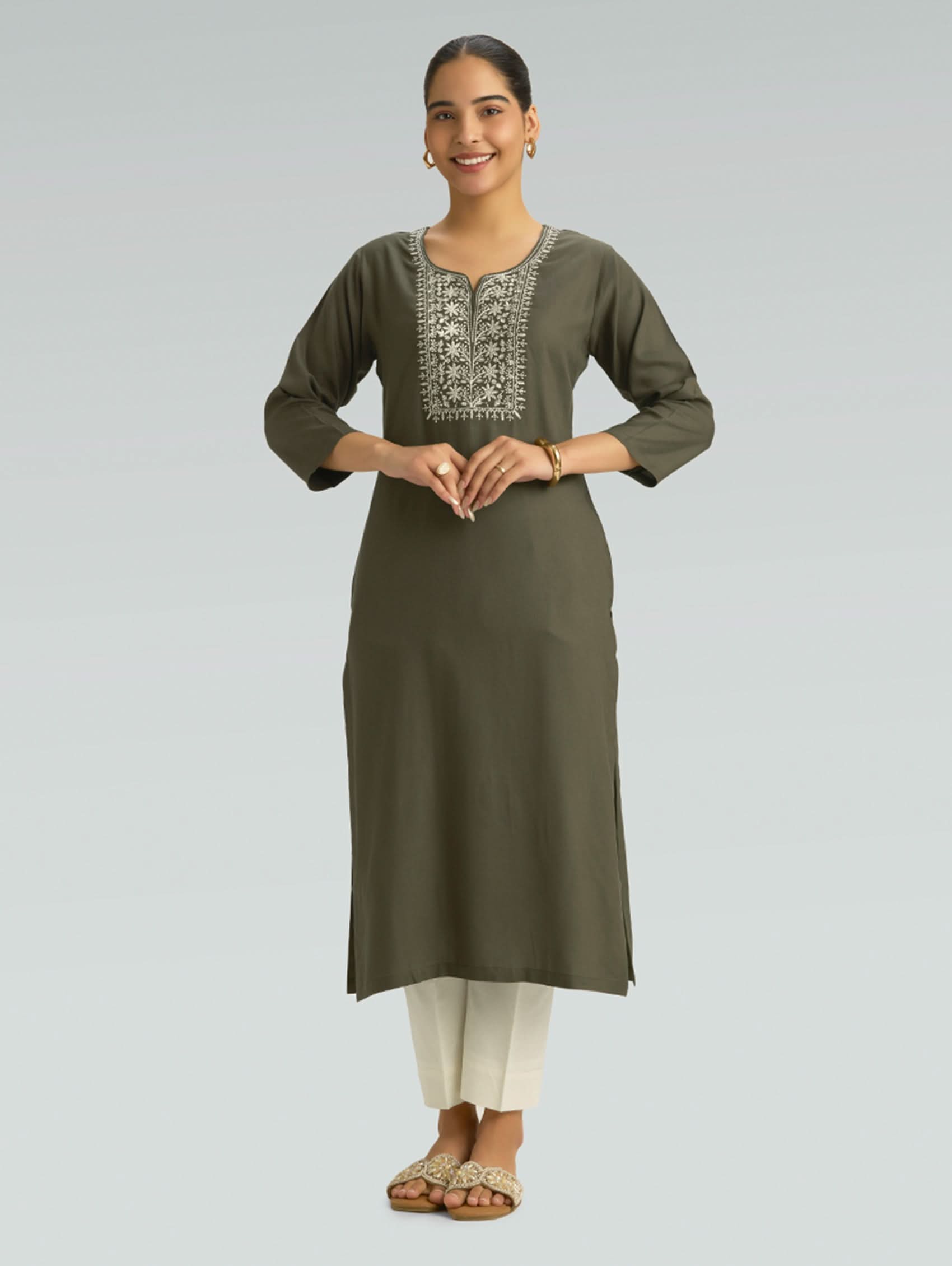 Woman wearing an olive green kurta with white pants on a light gray background