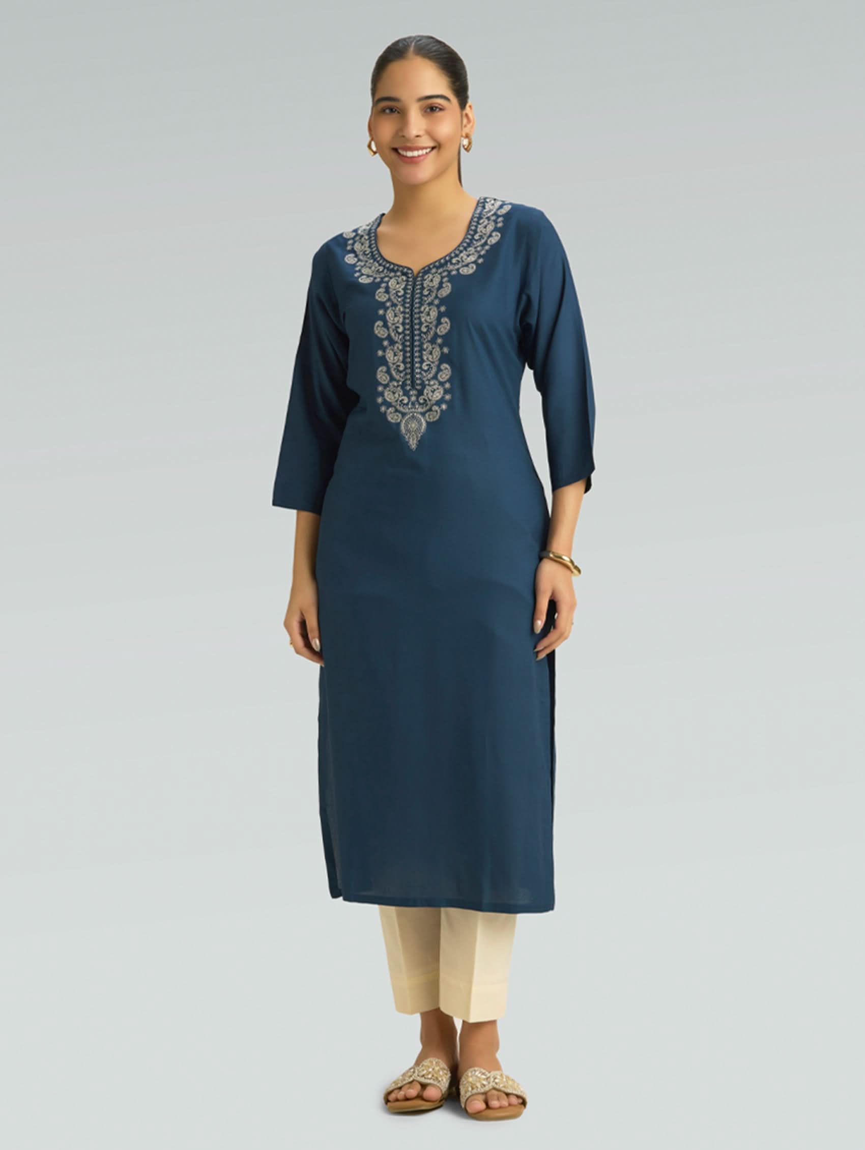 Woman wearing a blue embroidered kurta with beige pants on a gray background