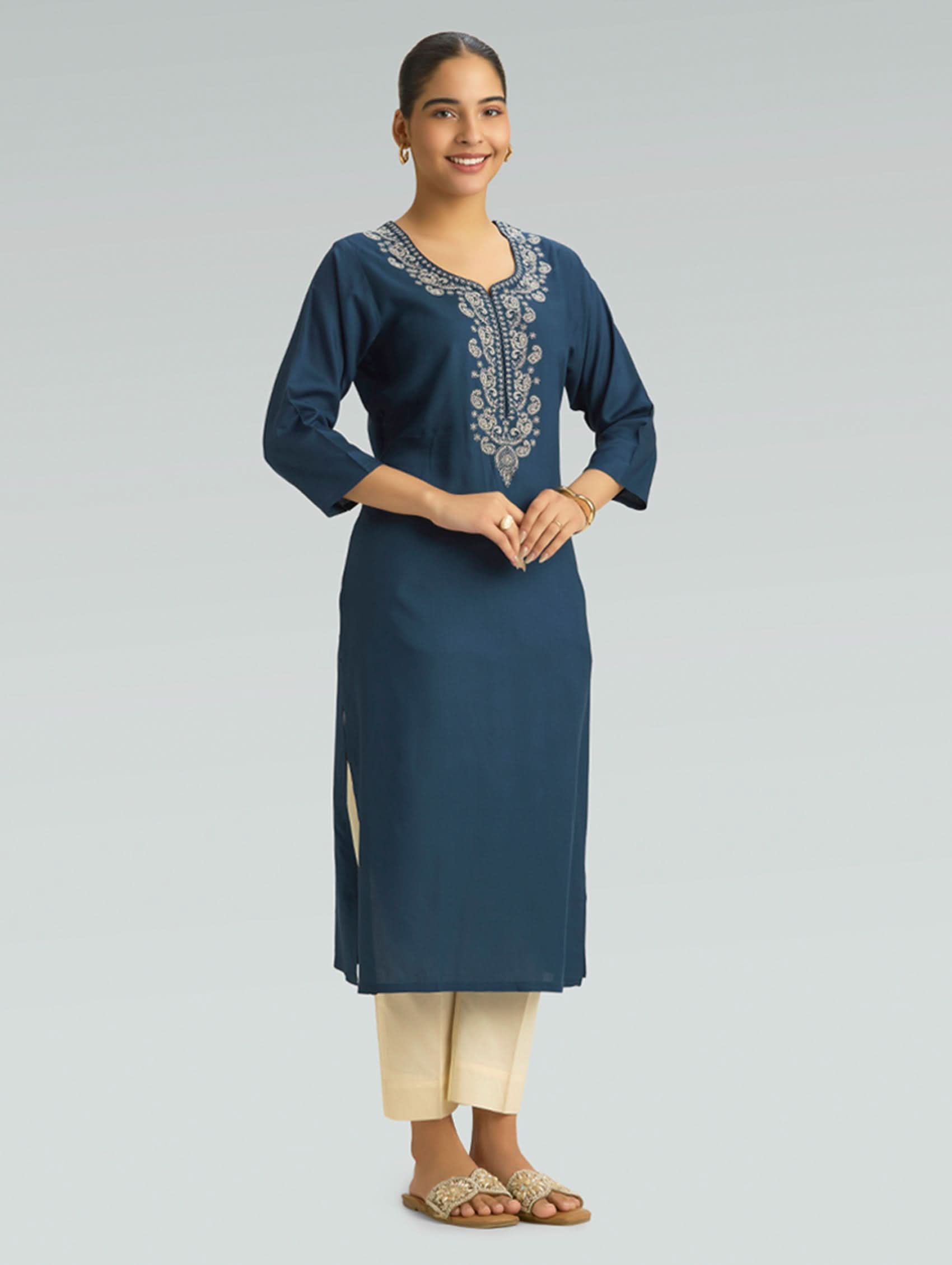Woman wearing a blue embroidered kurta with beige pants on a gray background