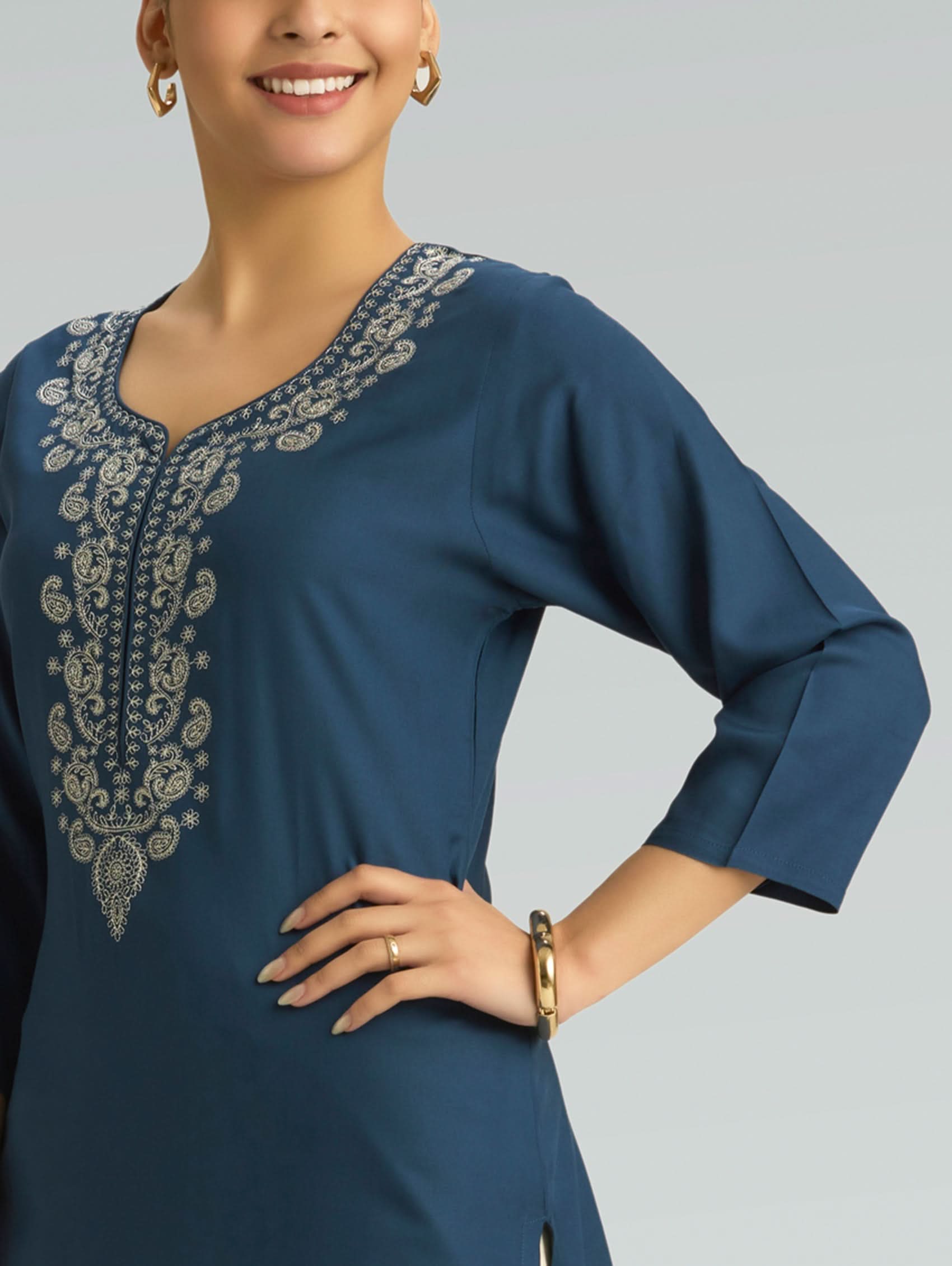 Woman wearing a blue dress with intricate silver embroidery on a gray background