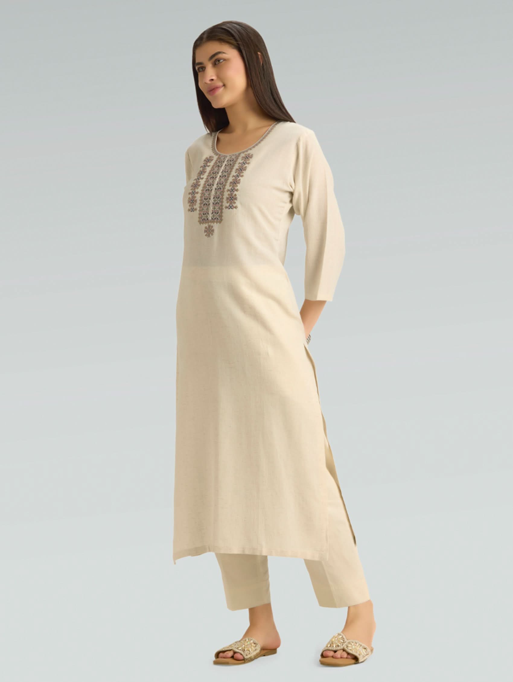 Woman wearing a beige kurta with embroidery on a light gray background