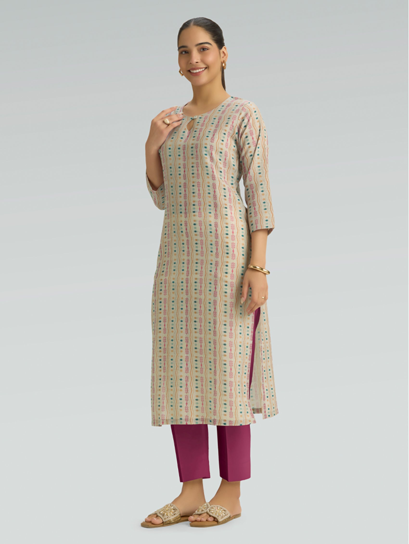 Woman wearing a patterned kurta with maroon pants on a light gray background