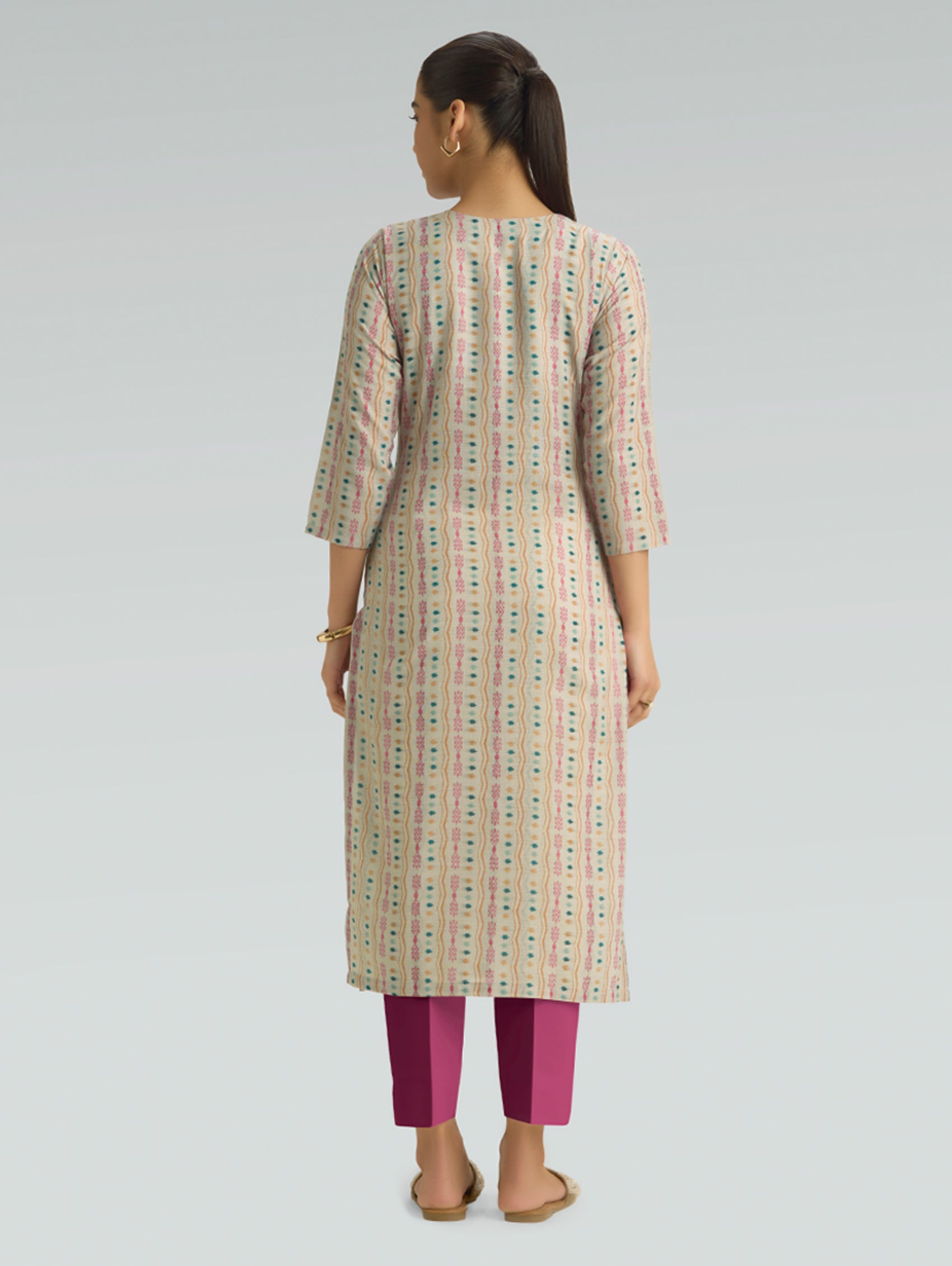 Woman wearing a patterned kurta with pink pants on a gray background