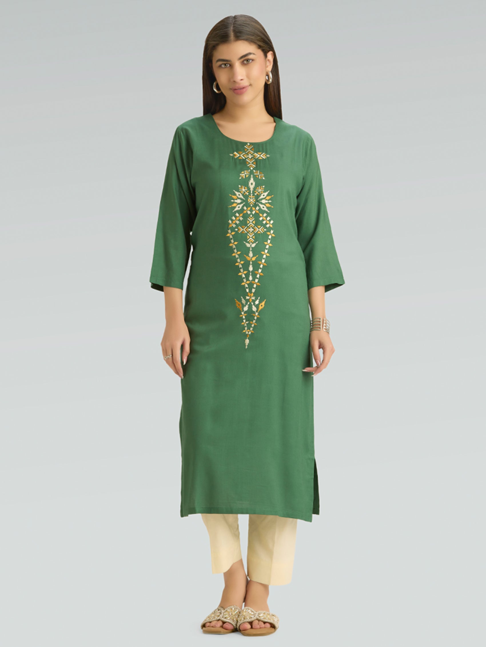 Woman wearing a green kurta with gold embroidery on a gray background