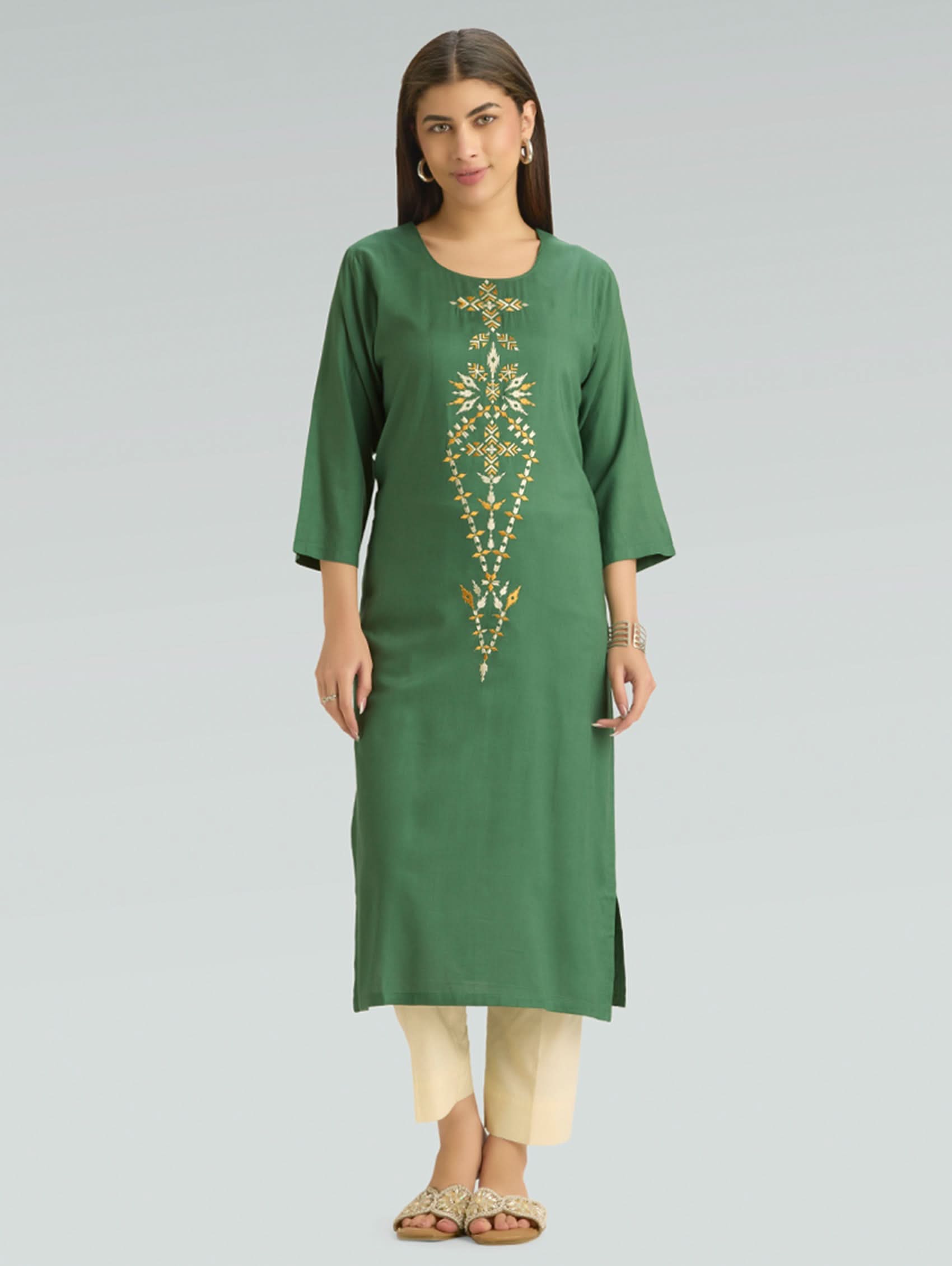 Woman wearing a green kurta with gold embroidery on a gray background
