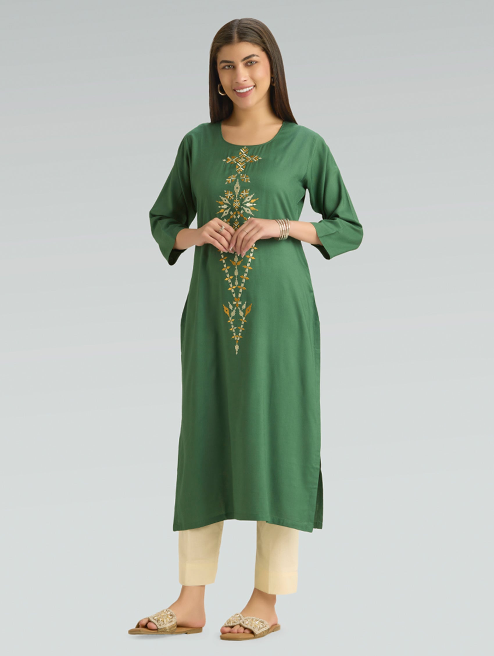 Woman wearing a green embroidered kurta with beige pants on a gray background