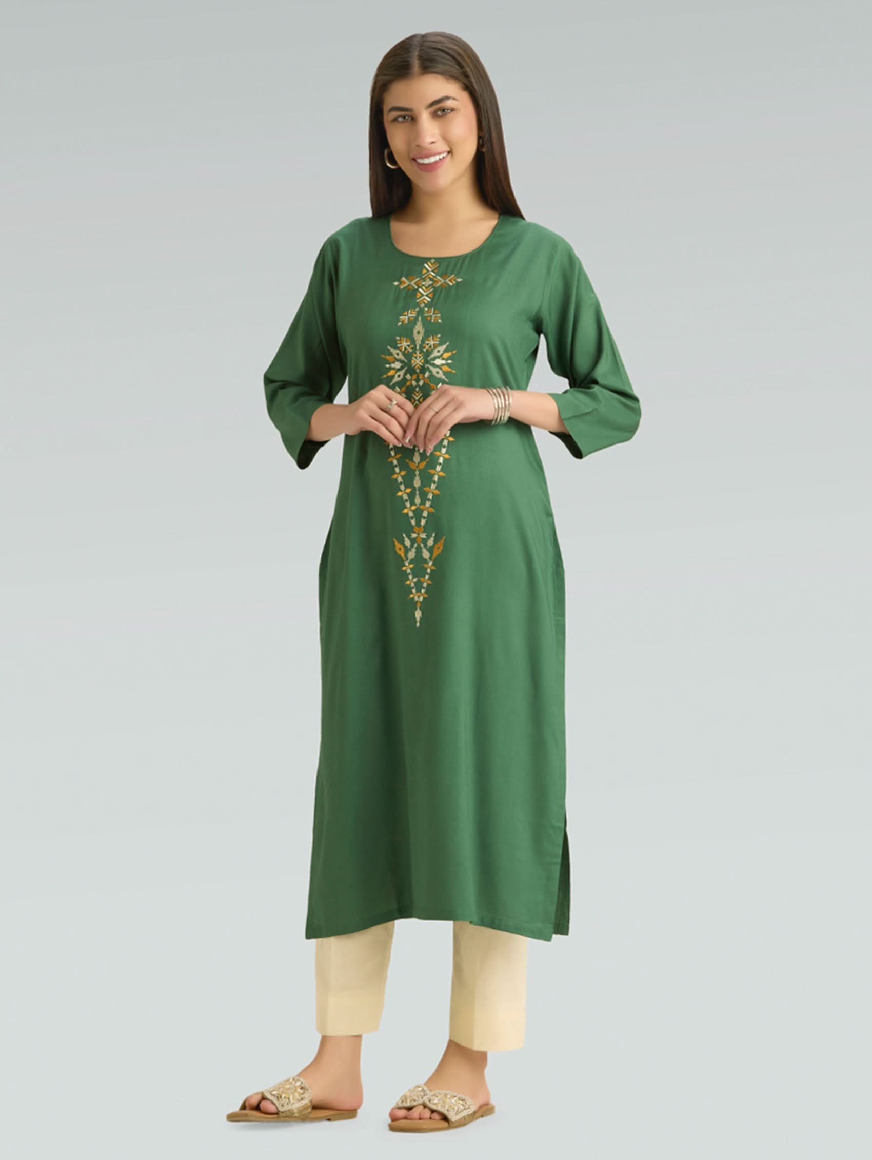 Woman wearing a green embroidered kurta with beige pants on a gray background