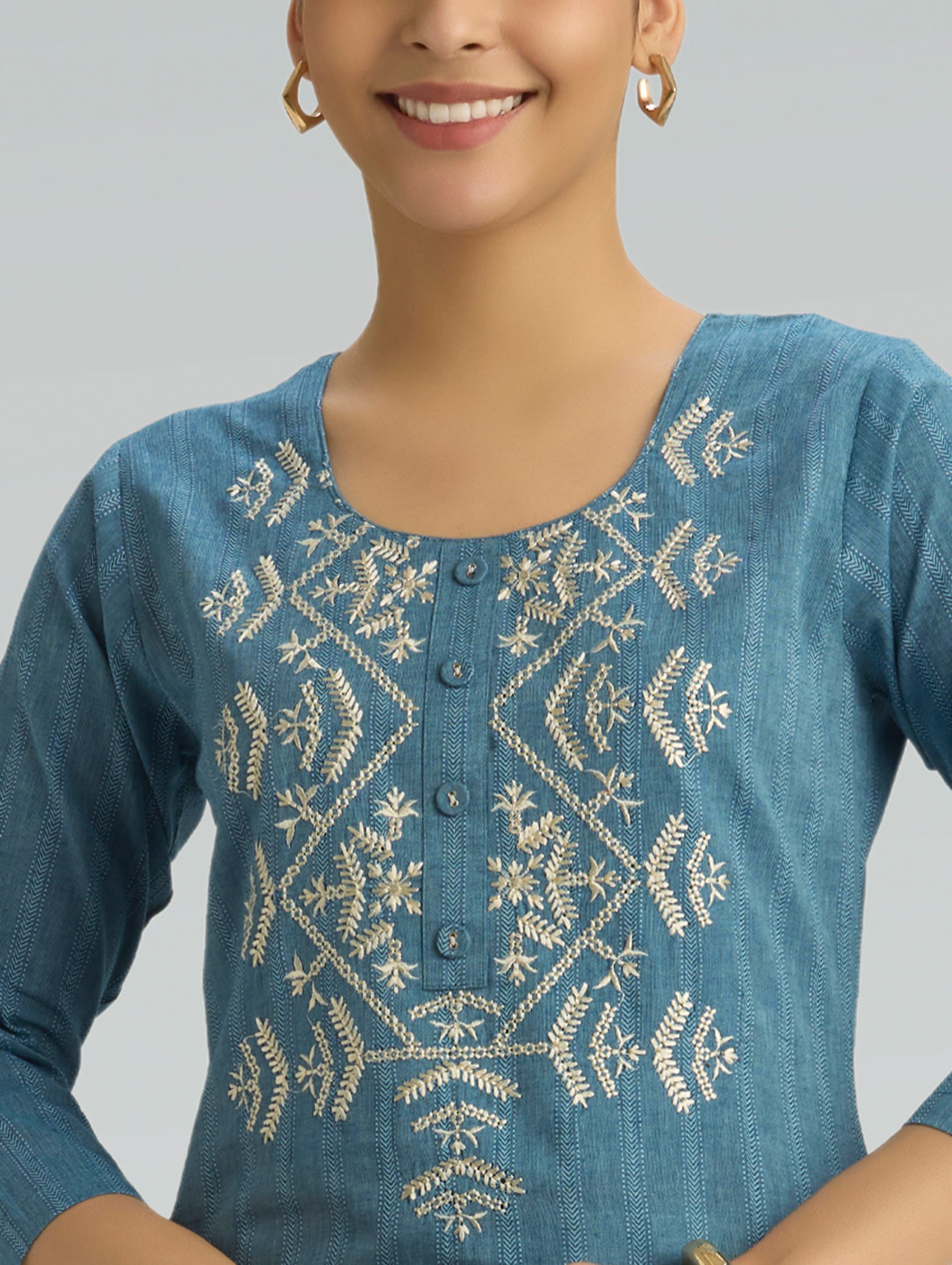 Woman wearing a blue embroidered top with a plain background