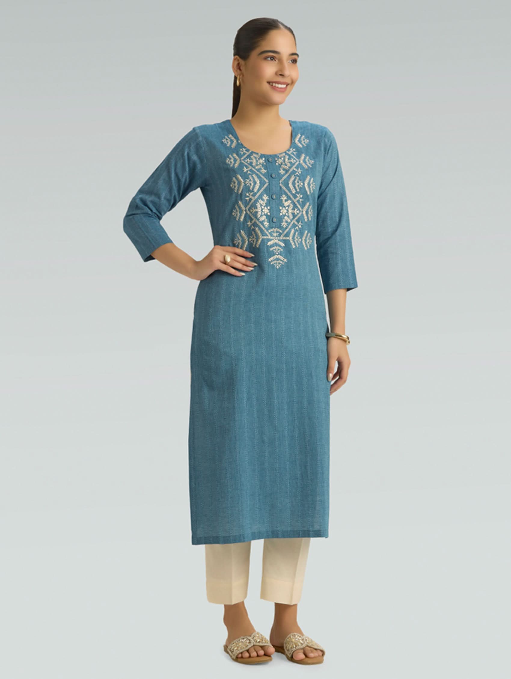 Woman wearing a blue embroidered kurta with beige pants on a gray background