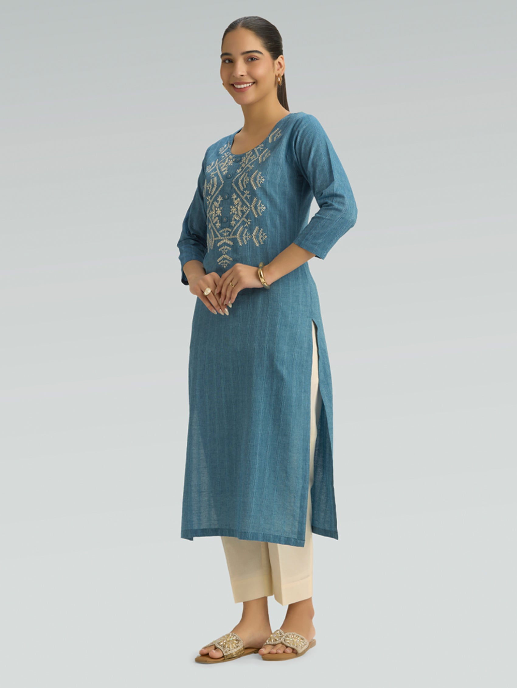 Woman wearing a blue embroidered kurta with beige pants on a gray background