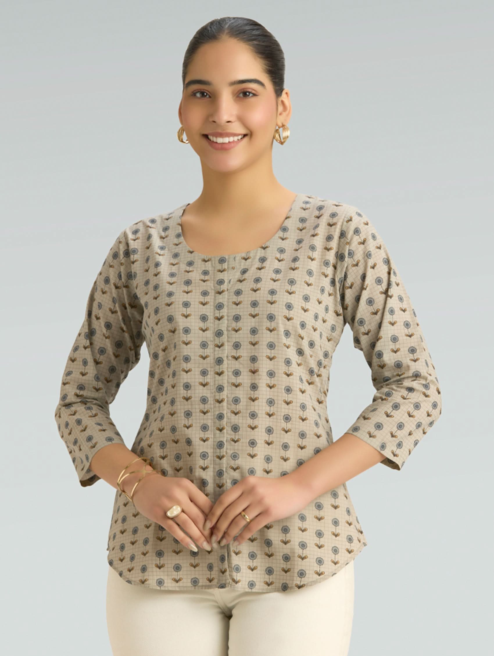 Woman wearing a patterned beige top on a gray background