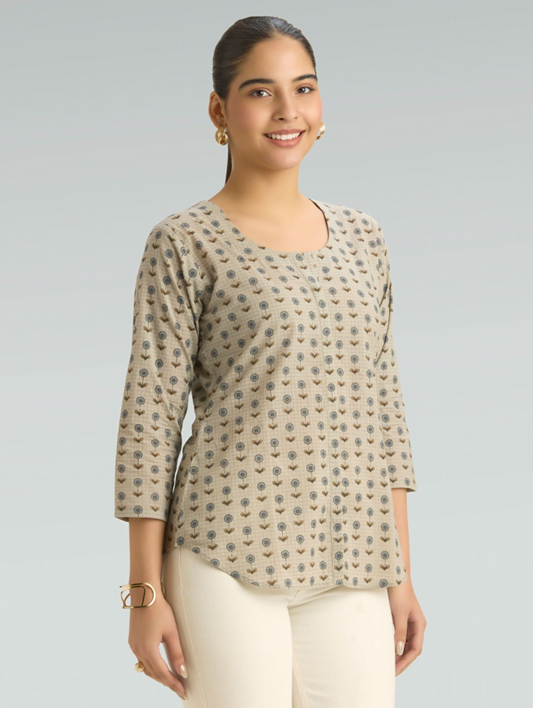 Woman wearing a patterned beige top against a gray background