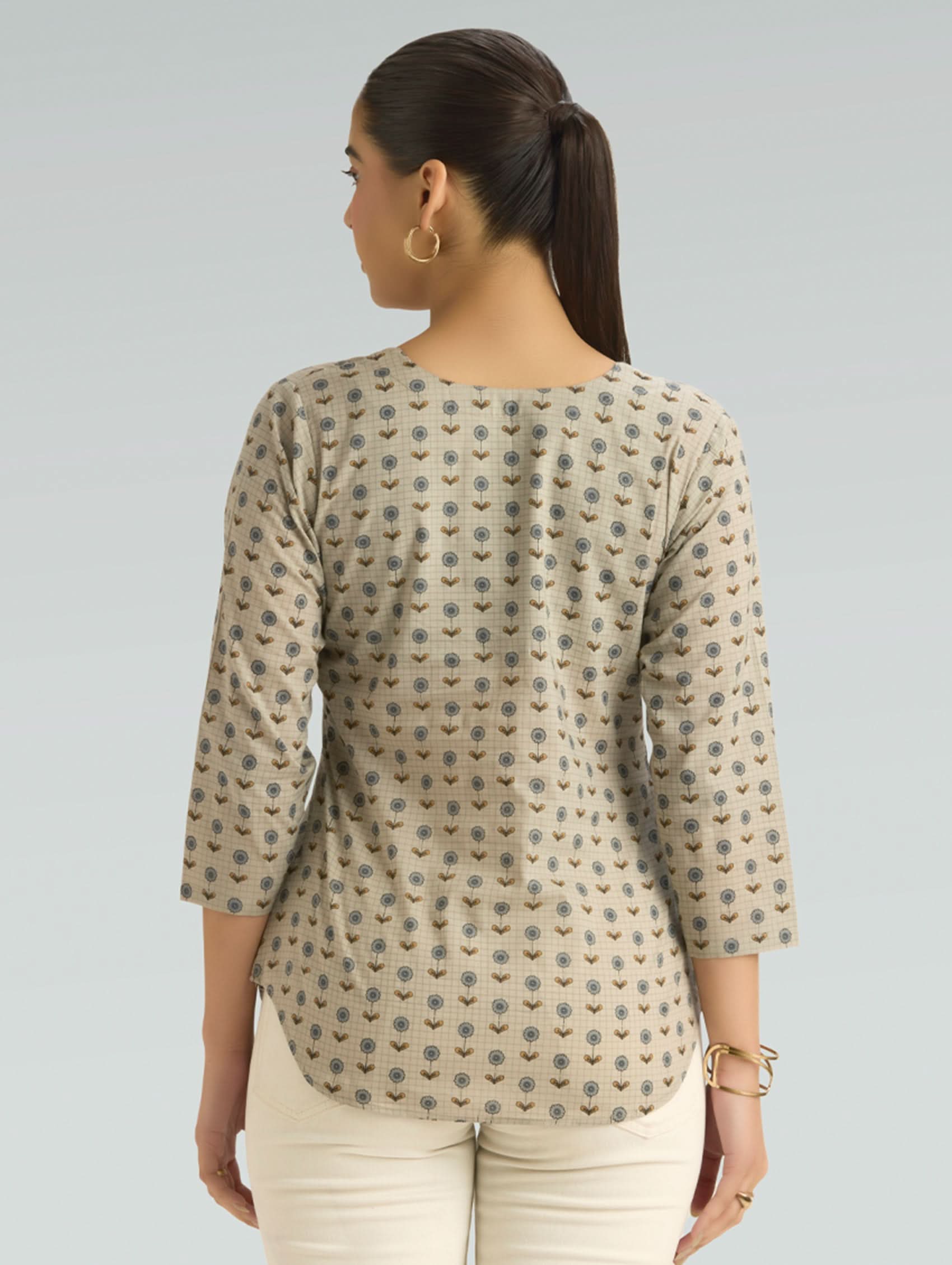 Woman wearing a patterned beige top on a plain background
