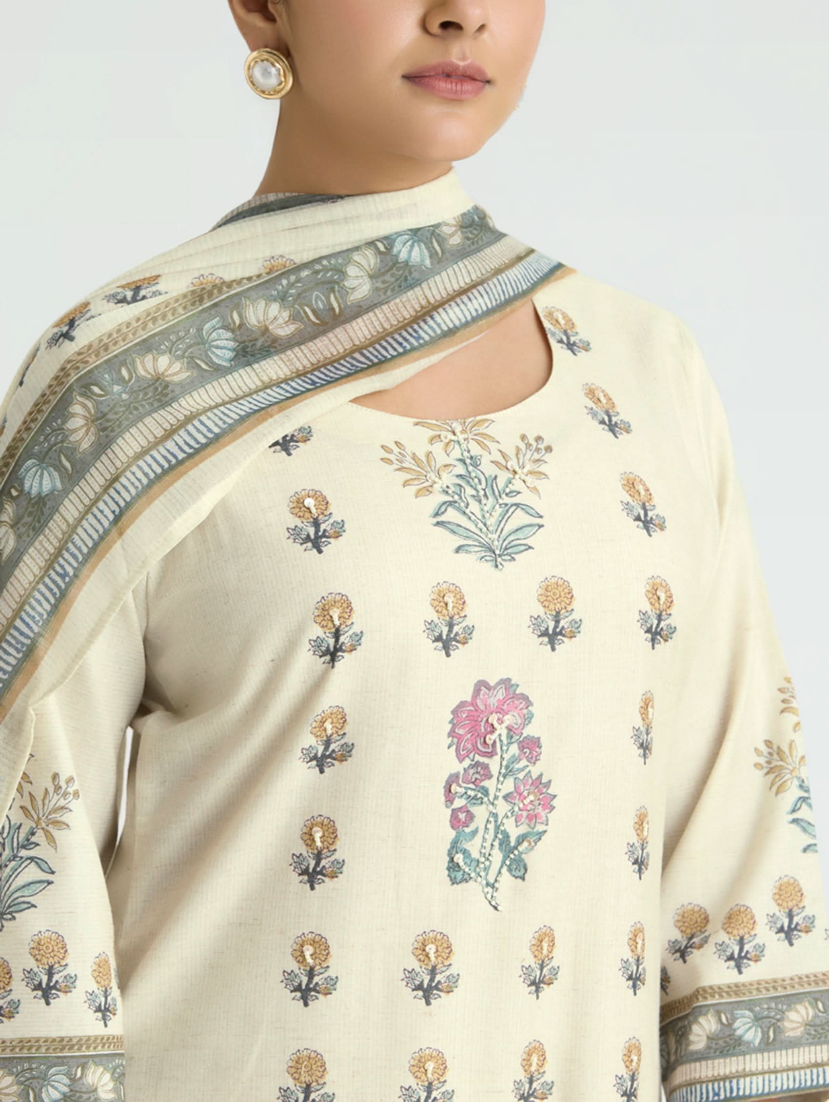 Woman wearing a cream saree with floral patterns and a matching blouse.