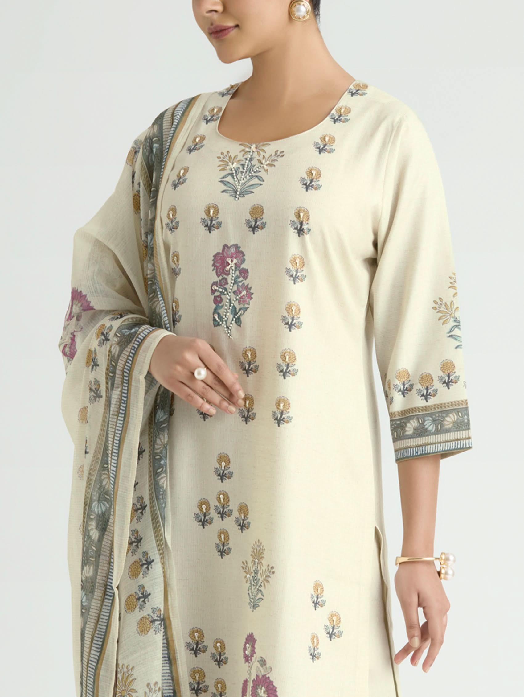 Woman wearing a cream-colored embroidered saree with a plain background