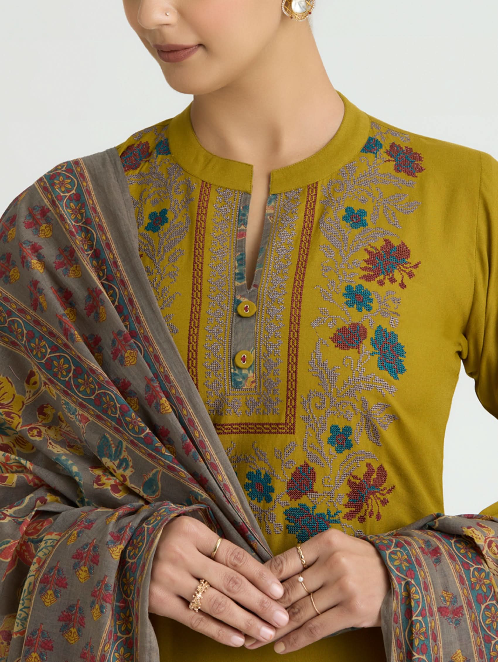 Woman wearing a green embroidered top with a patterned shawl on a white background