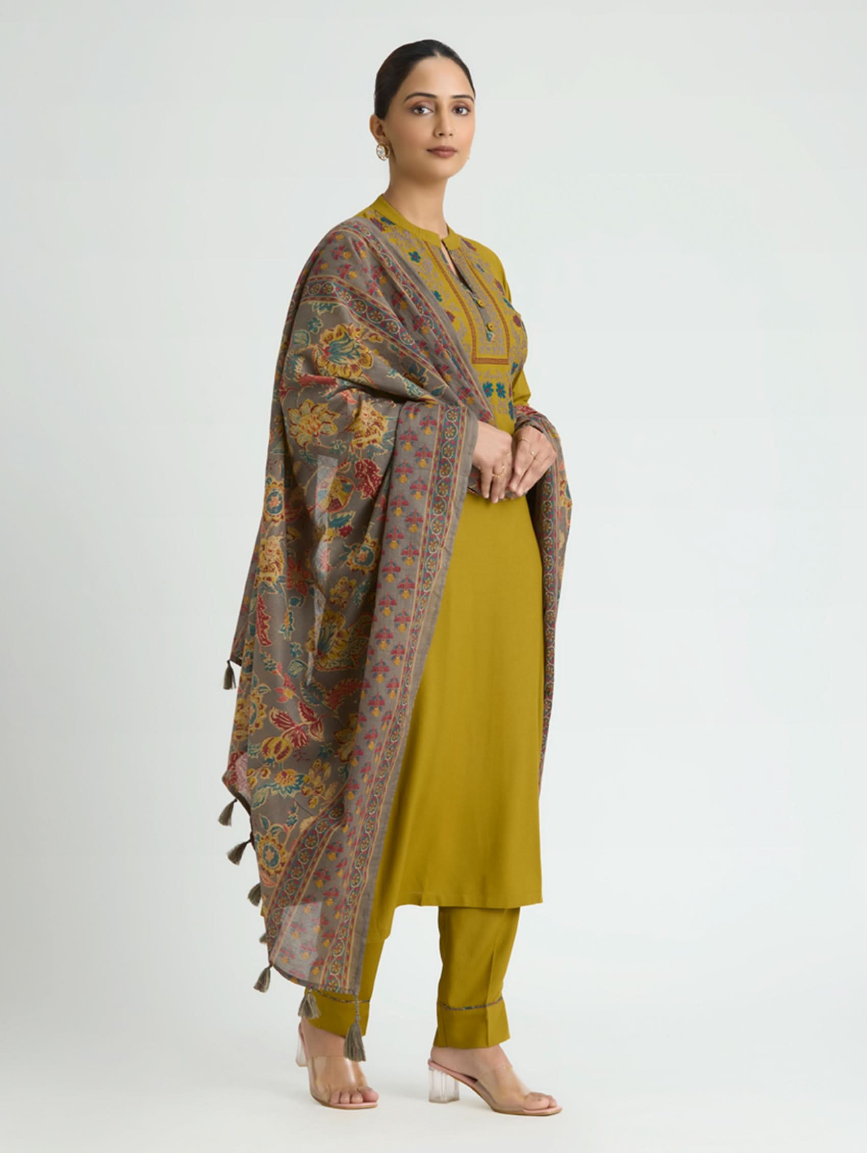 Woman wearing a mustard yellow outfit with a patterned shawl on a white background