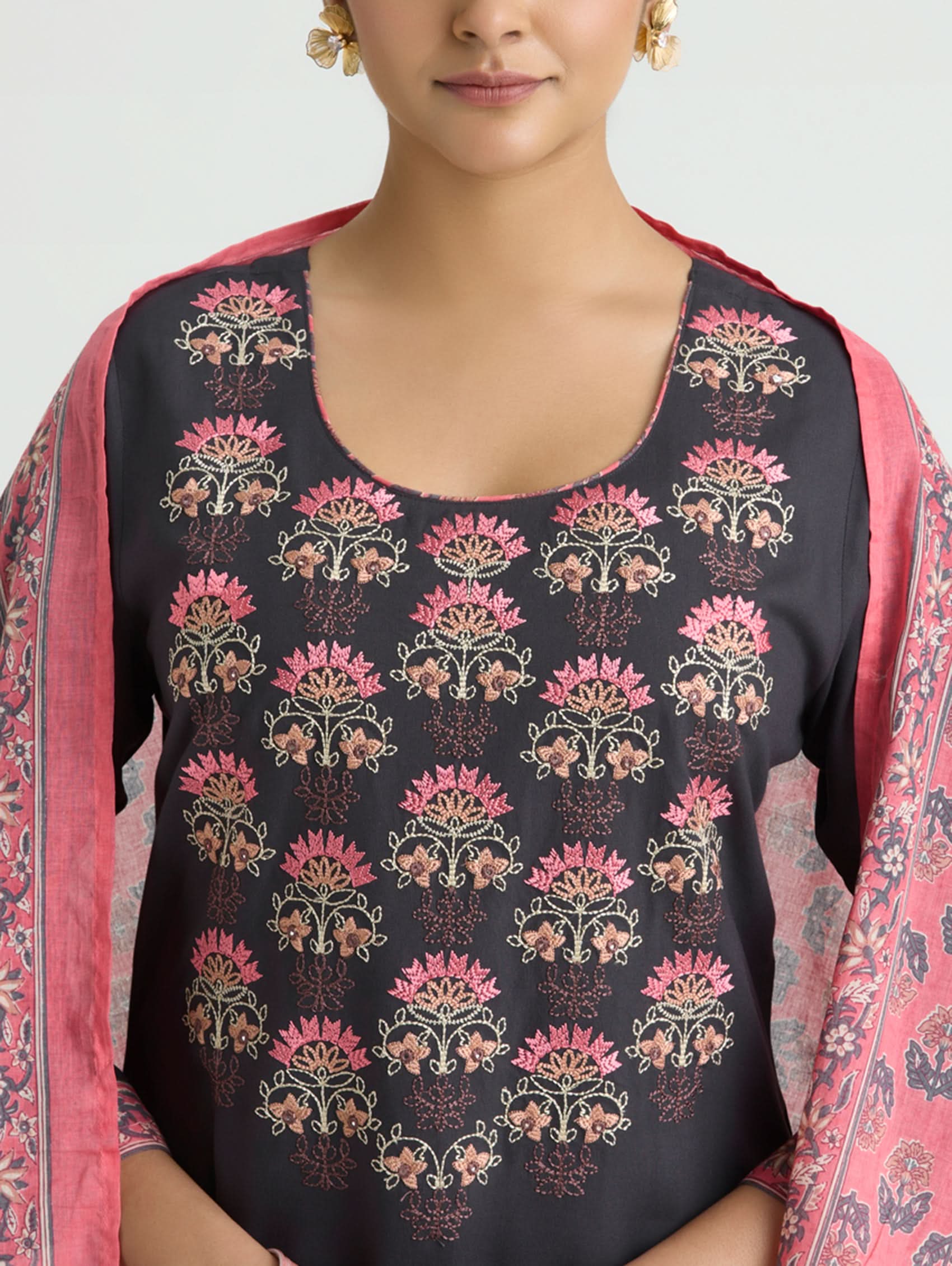 Woman wearing a black top with pink floral pattern and pink dupatta on a light gray background
