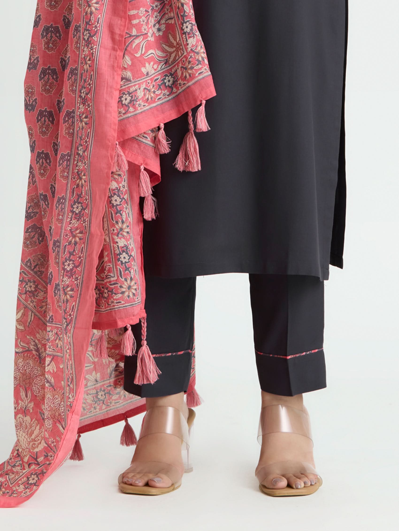 Person wearing a black outfit with a pink patterned scarf draped over the shoulder on a white background