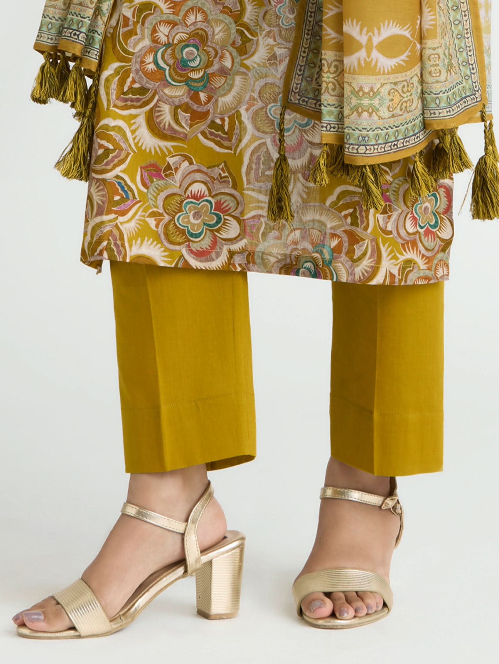Traditional outfit with a patterned top and yellow pants, paired with gold sandals on a white background.
